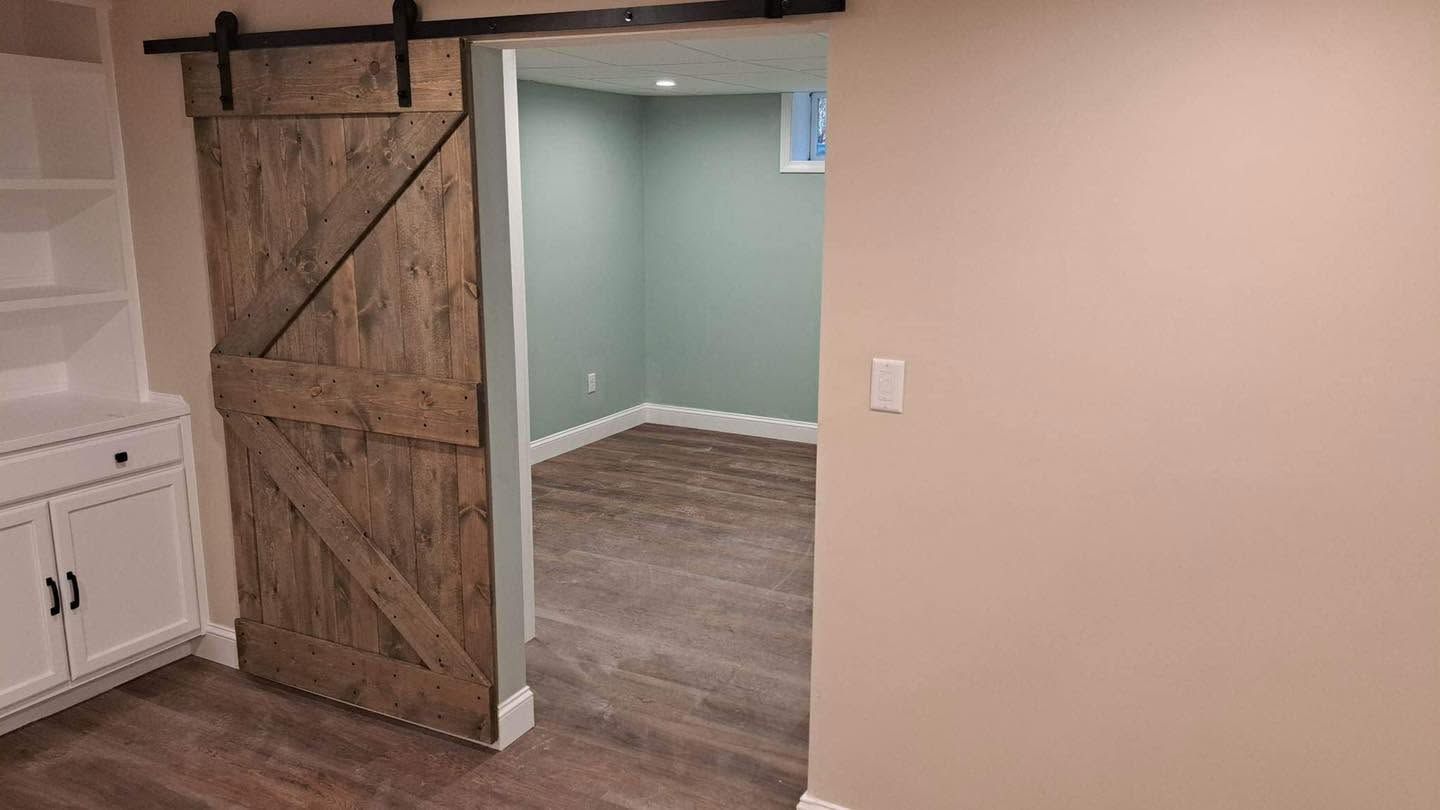 Interior room with sliding barn door, white cabinets, and a doorway to a gray-floored room