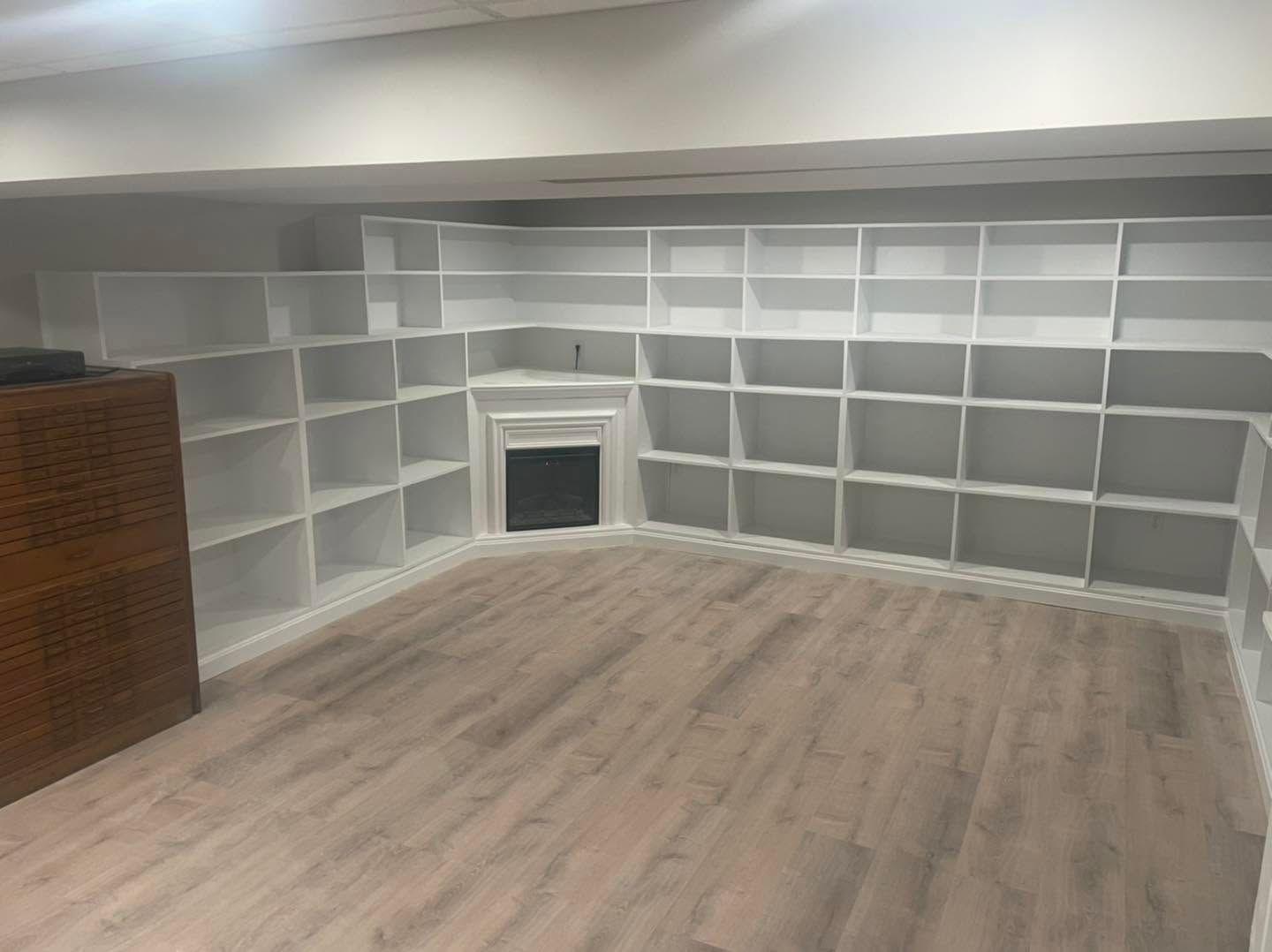 Built-in white bookshelves and gray fireplace in an empty room with light wood flooring