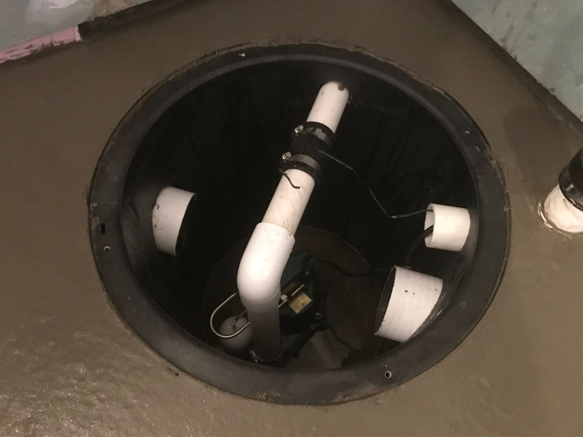 Round black floor opening with white PVC pipes and electrical wiring inside