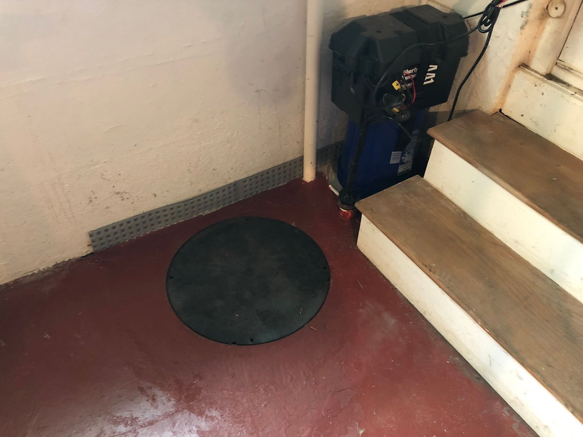 Dim stairwell with a red floor, black round mat, white steps, and a blue bag by the stairs.