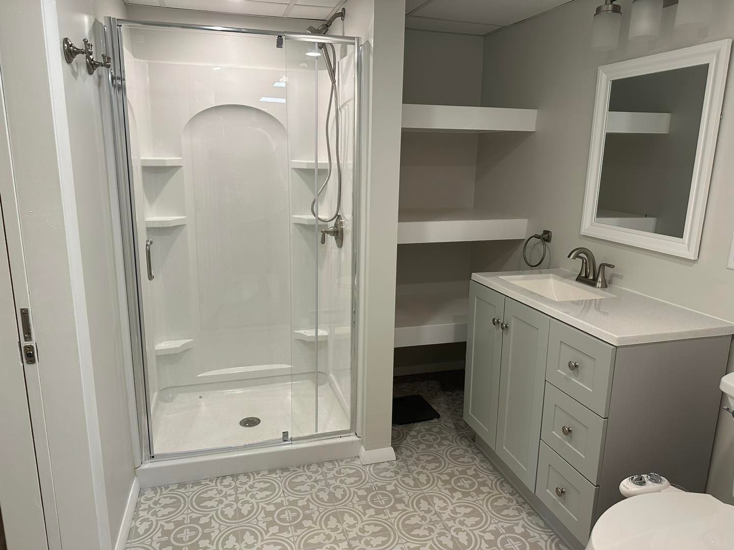 Bathroom with walk-in shower, vanity, mirror, and built-in shelves on a gray floor.