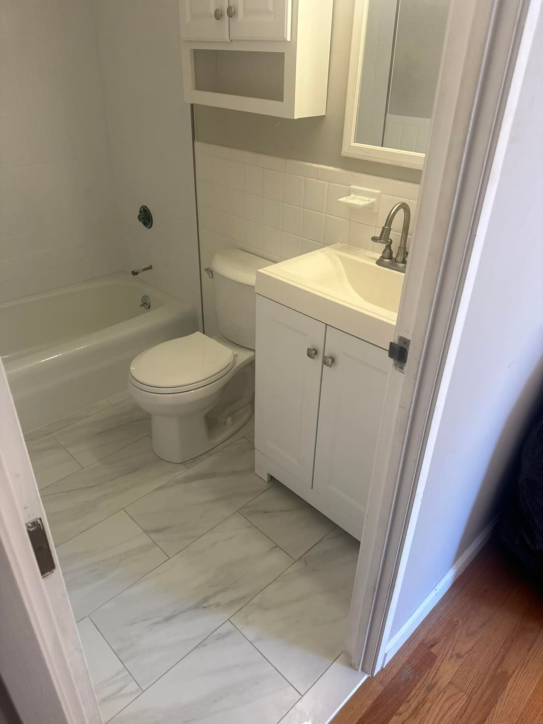 Small bathroom with tub, toilet, and white vanity, viewed from the doorway.