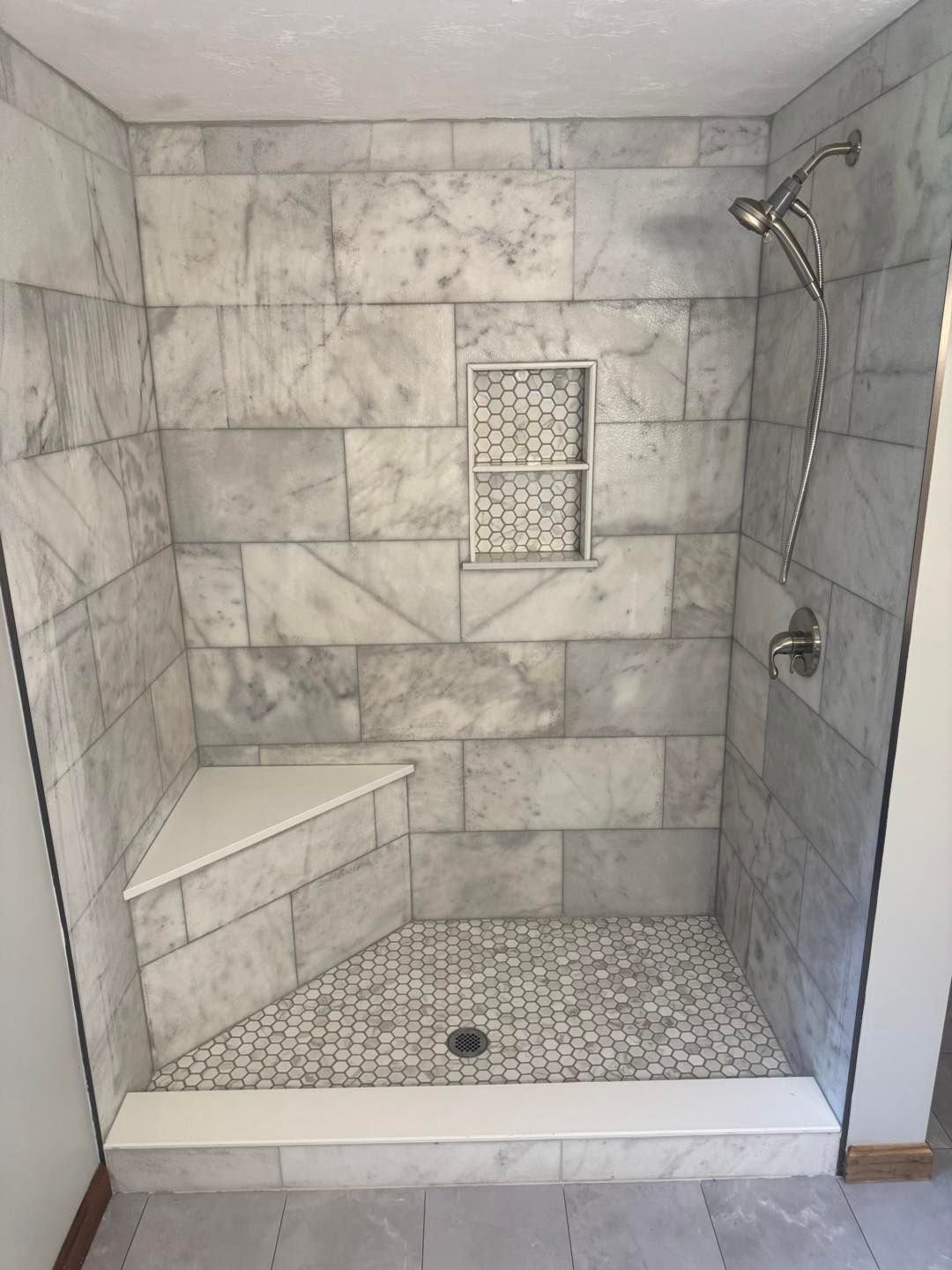 Stone-tiled walk-in shower with bench, mosaic floor, and rainfall showerhead