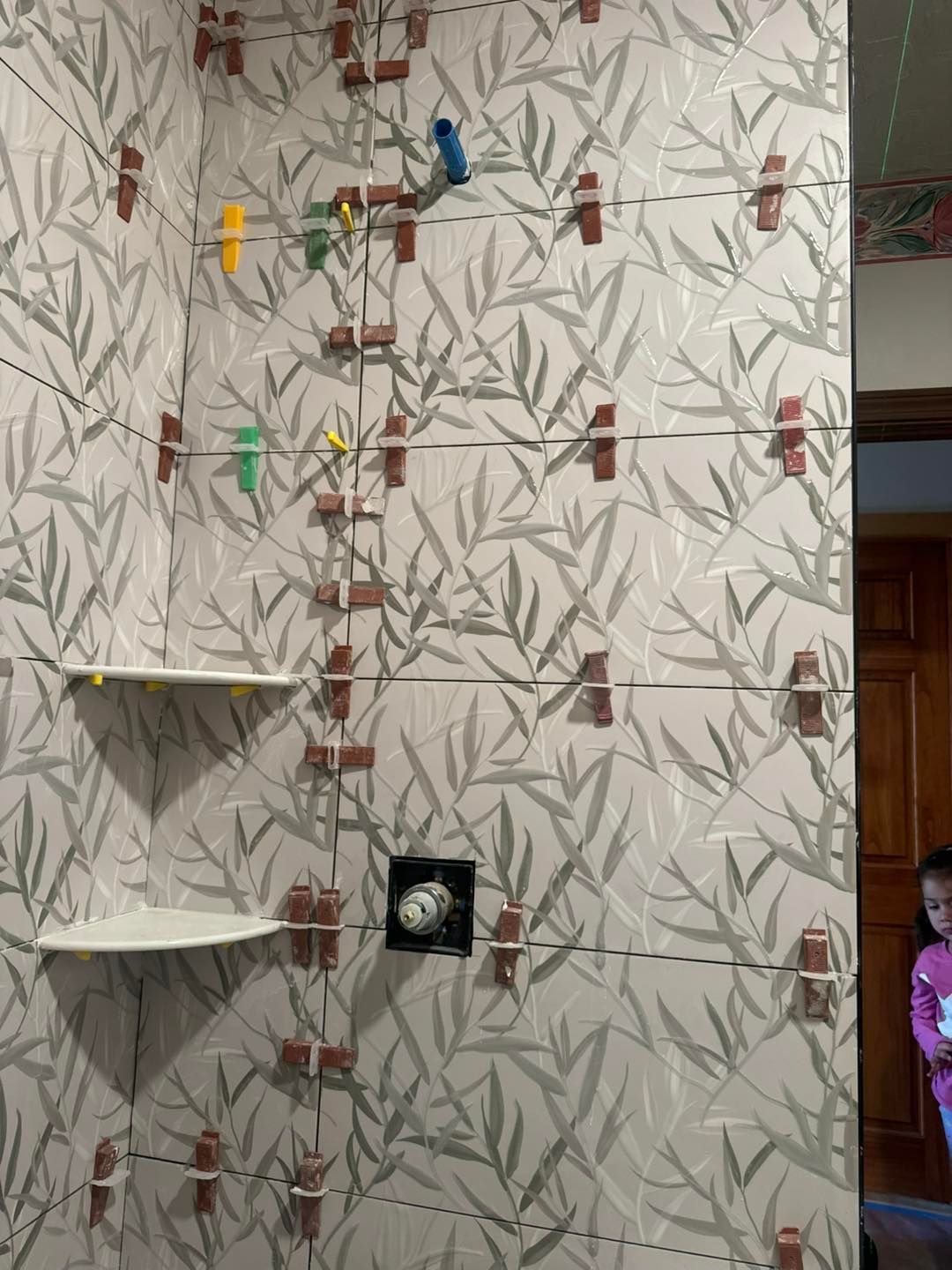Decorative wall with leaf wallpaper, hanging clothespins, shelves, and a small black square fixture.
