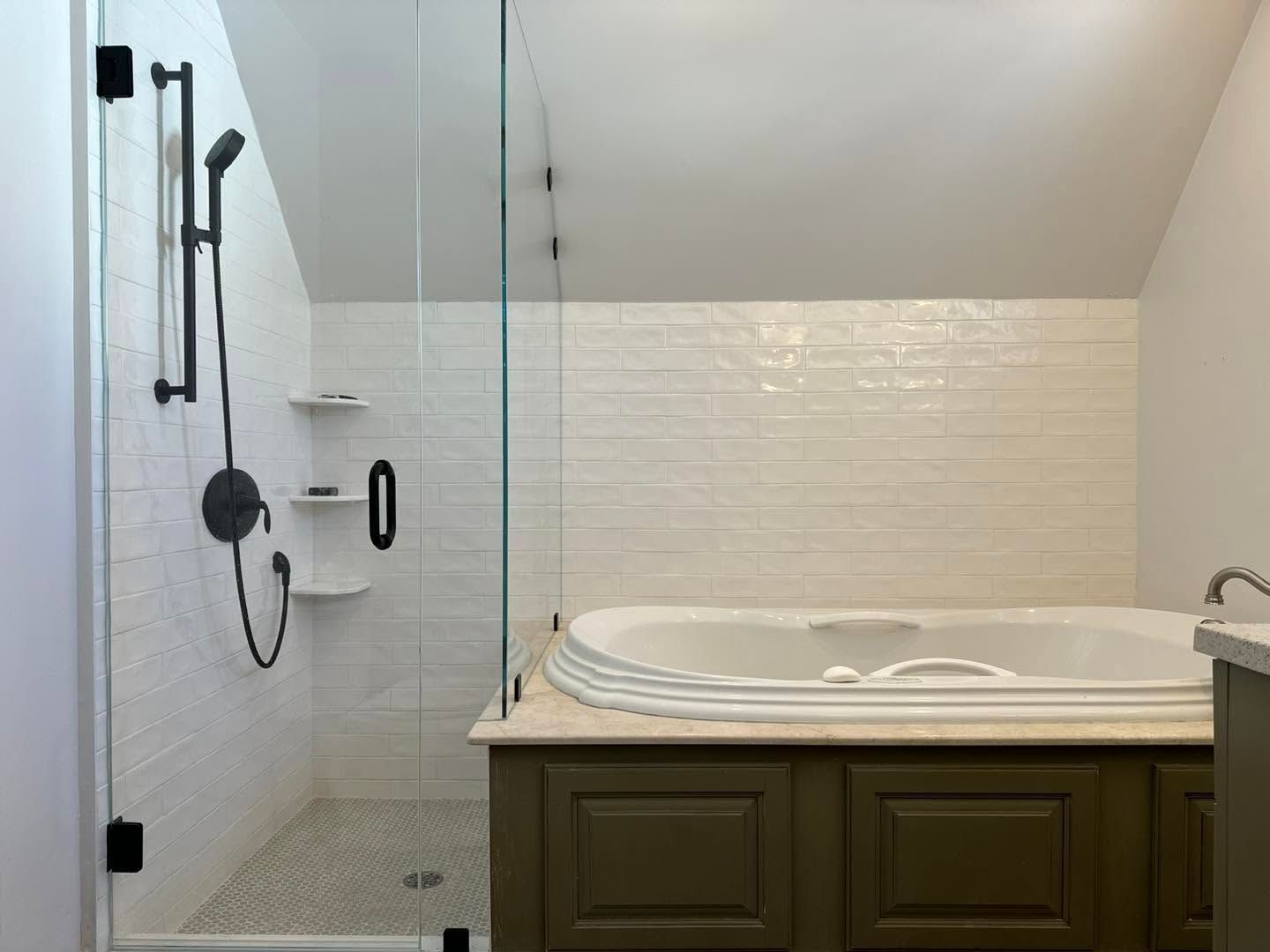 Accessible bathroom with walk-in shower, glass partition, grab bars, and white jacuzzi tub with dark vanity cabinetry