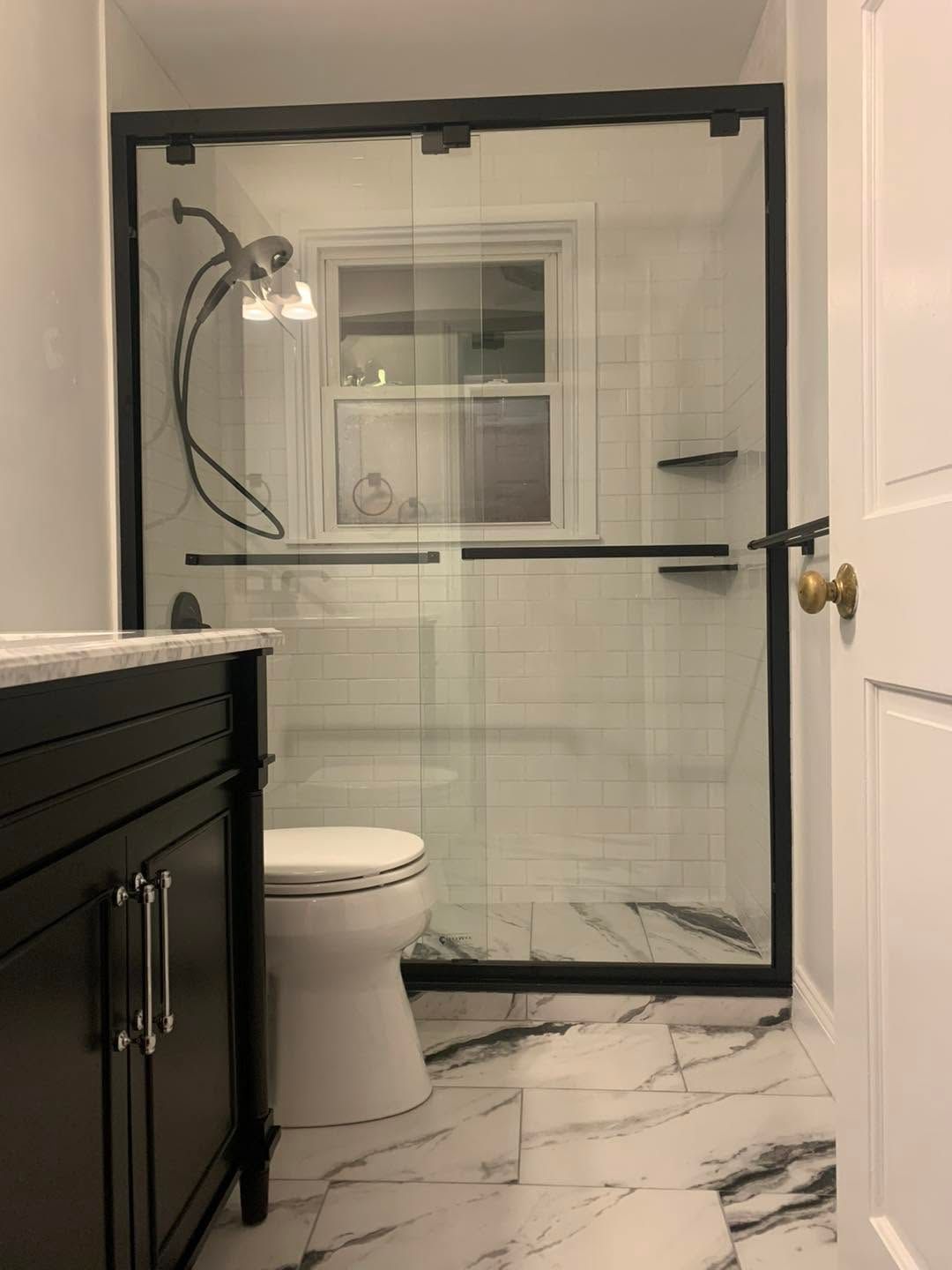 Bathroom with black-framed glass shower, toilet, vanity, and marble-look tile floor and walls