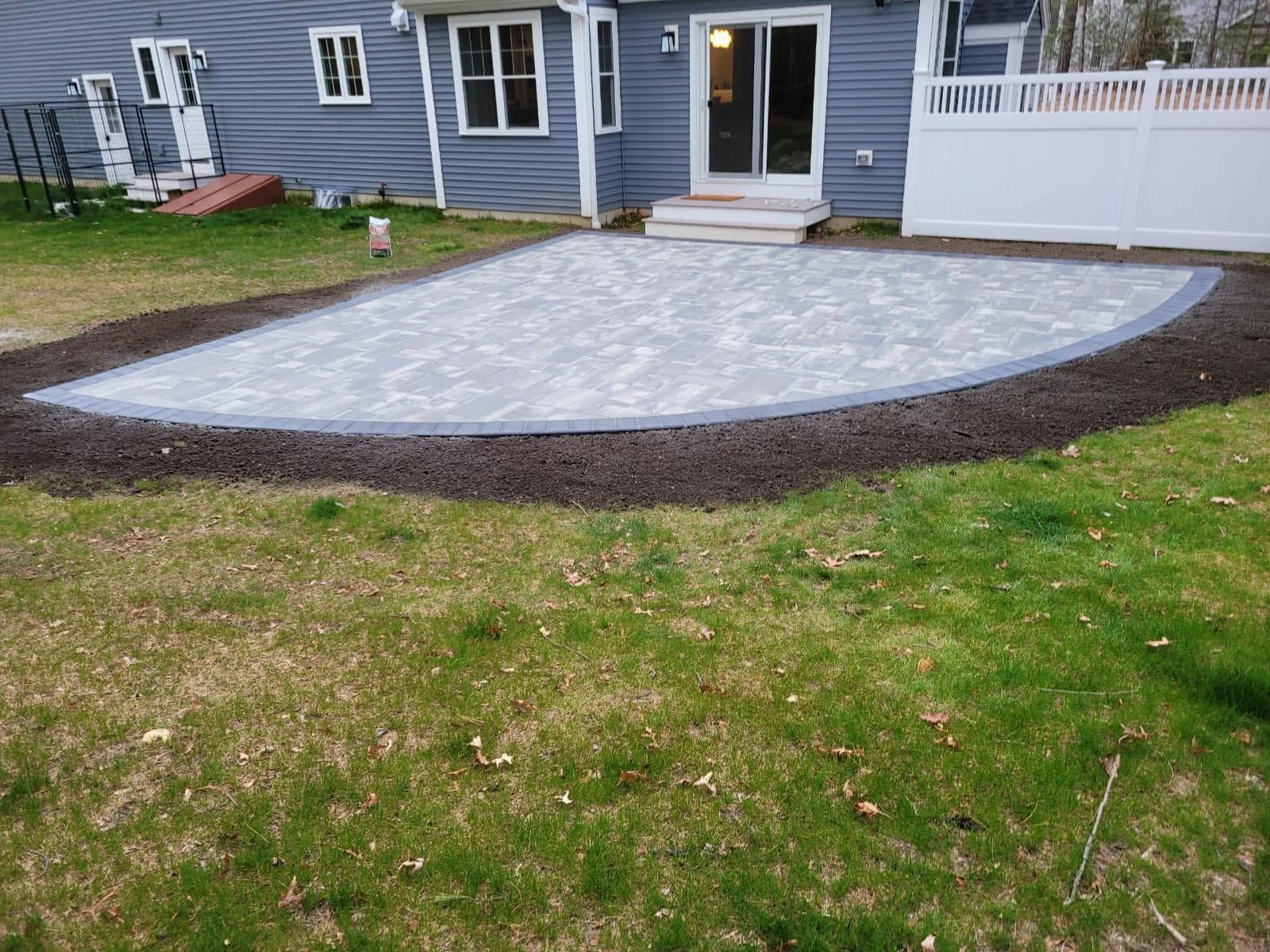Gray paver patio with dark edging in front of a house’s back door and white porch railings
