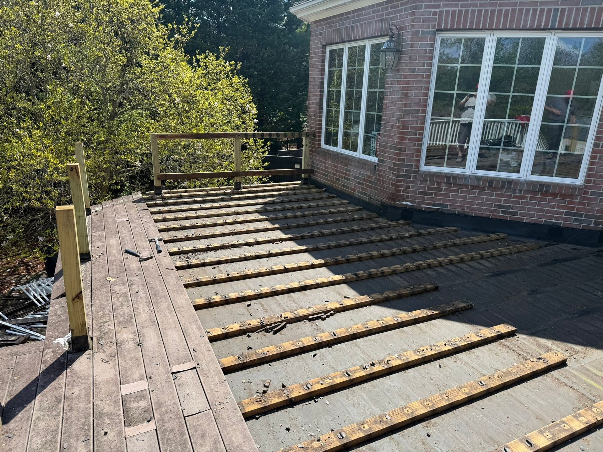 Backyard deck under construction beside a brick house, with joists laid across the frame.