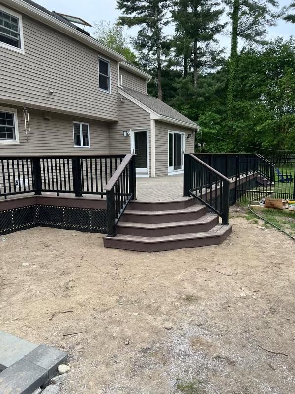 Back porch with brown steps, black railings, and a beige house exterior in a wooded yard