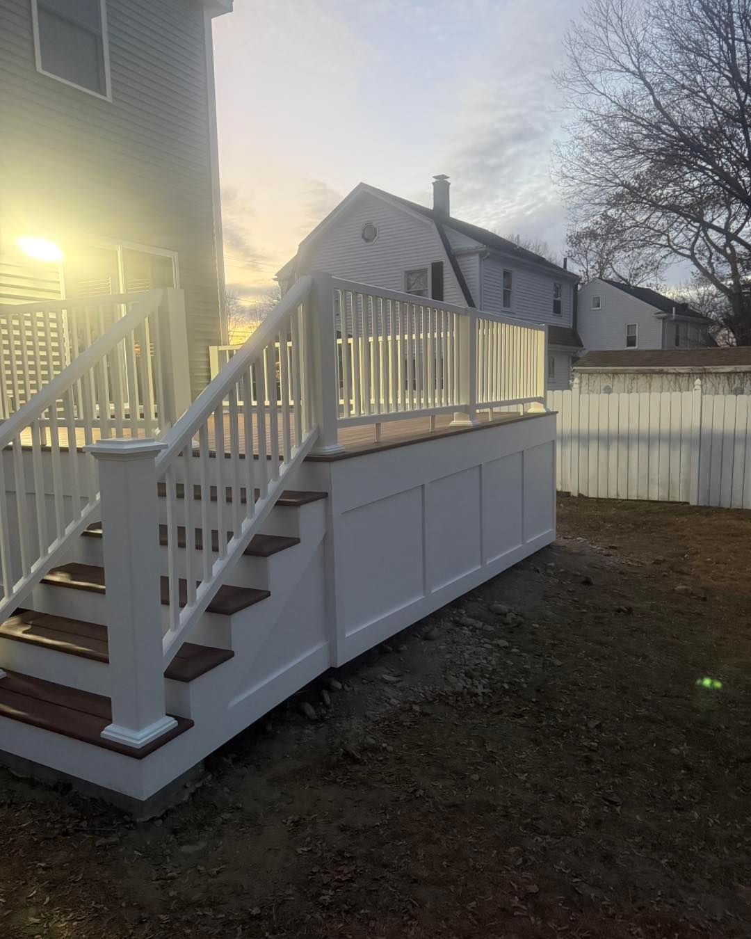 White wooden backyard deck with stairs beside a house at dusk