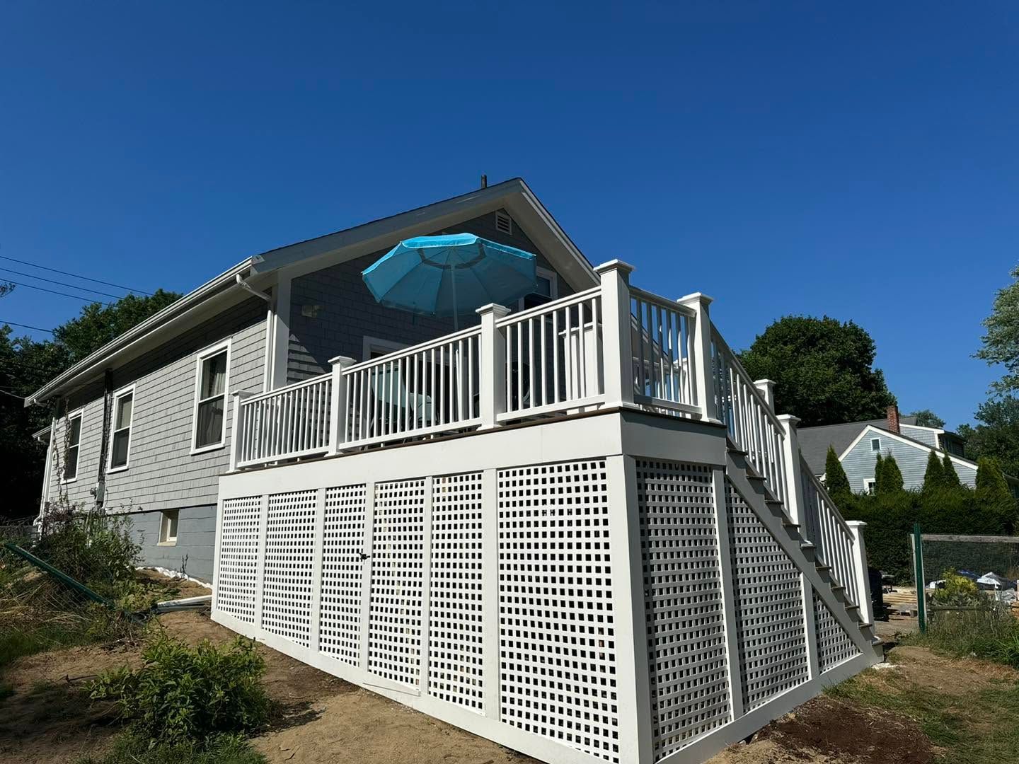 White house with raised deck, stairs, and blue umbrella under a clear sky