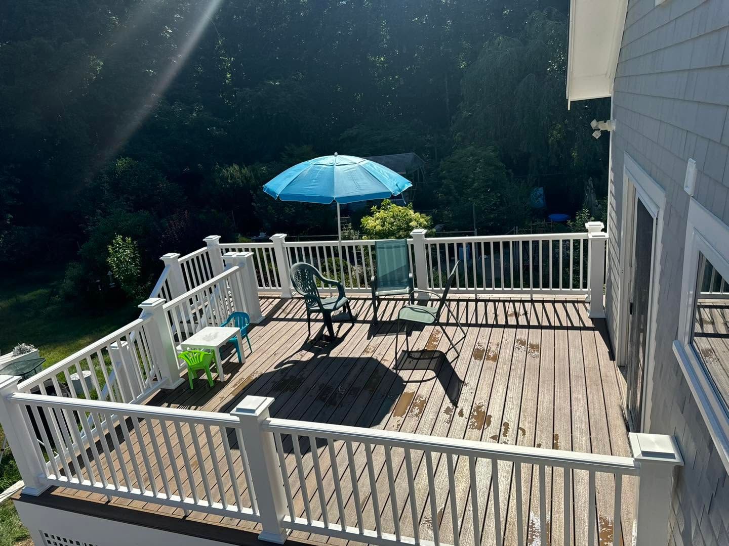 Wooden deck with white railing, patio table, and blue umbrella in a sunny backyard