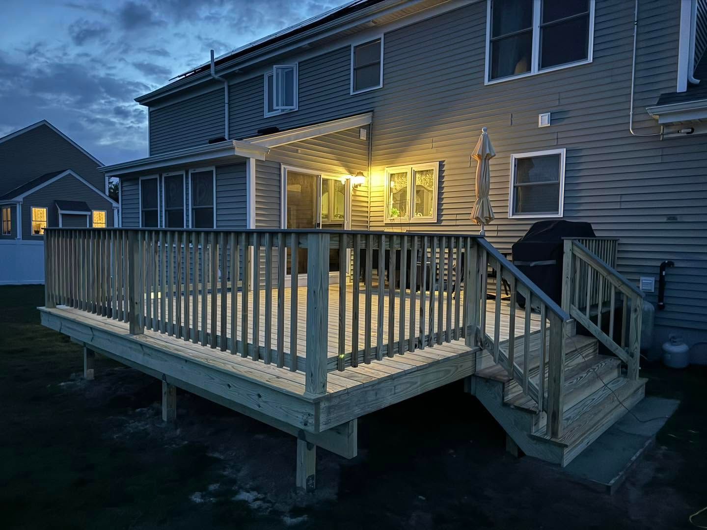 Back deck with white railing and stairs beside a house, leading to a stone patio and grassy yard