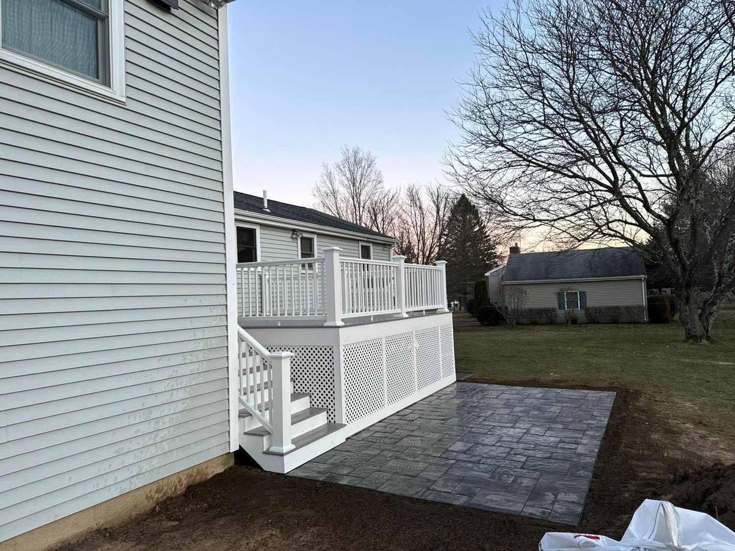 Backyard deck with white railing and stairs beside a house, overlooking a grassy yard at dusk