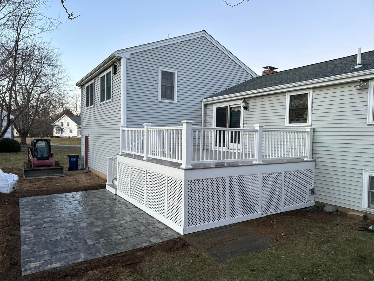 Backyard deck with white lattice railing, gray siding, and a paved patio beside a house