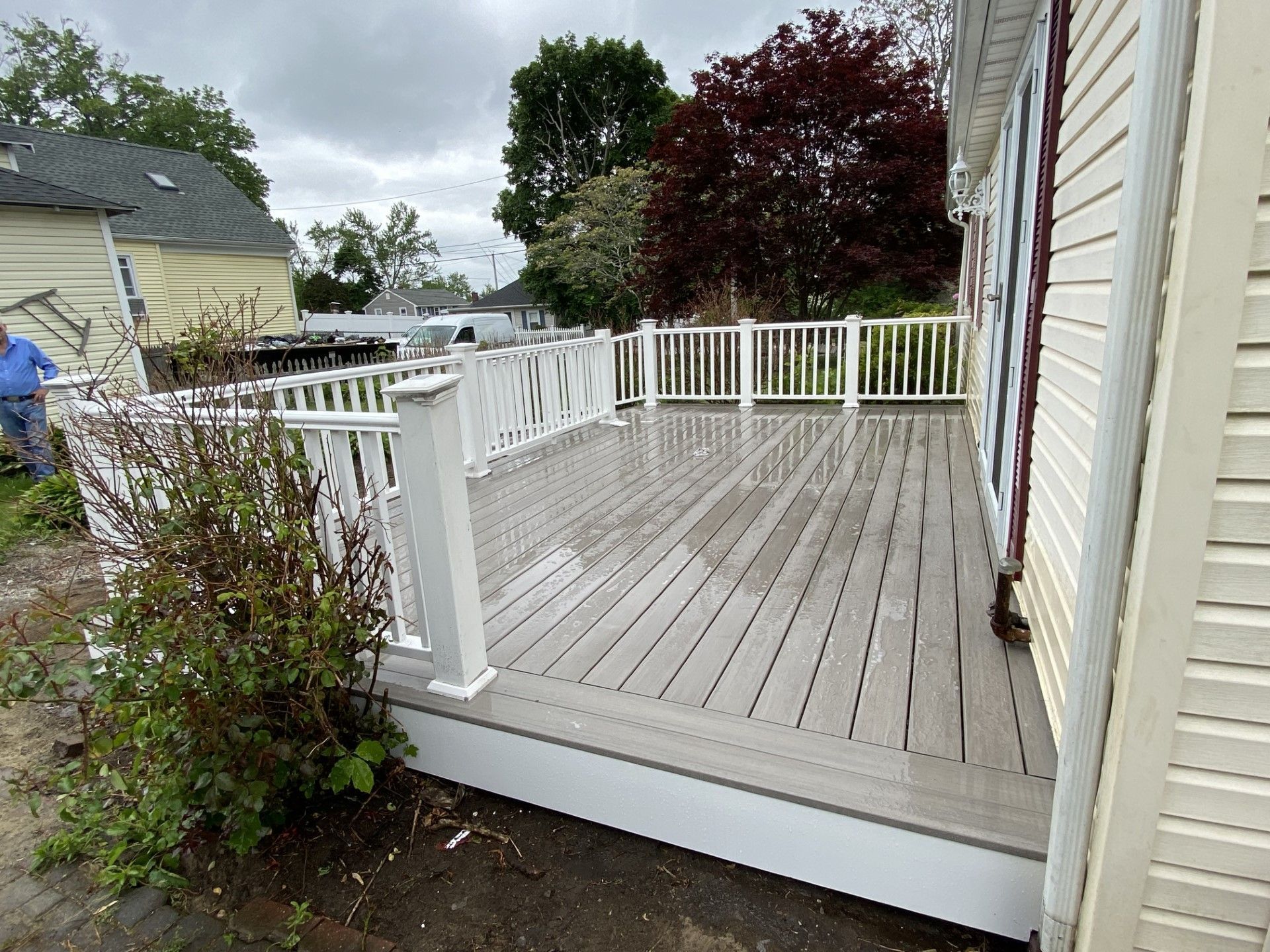 Small gray wooden deck with white railings beside a beige house on an overcast day