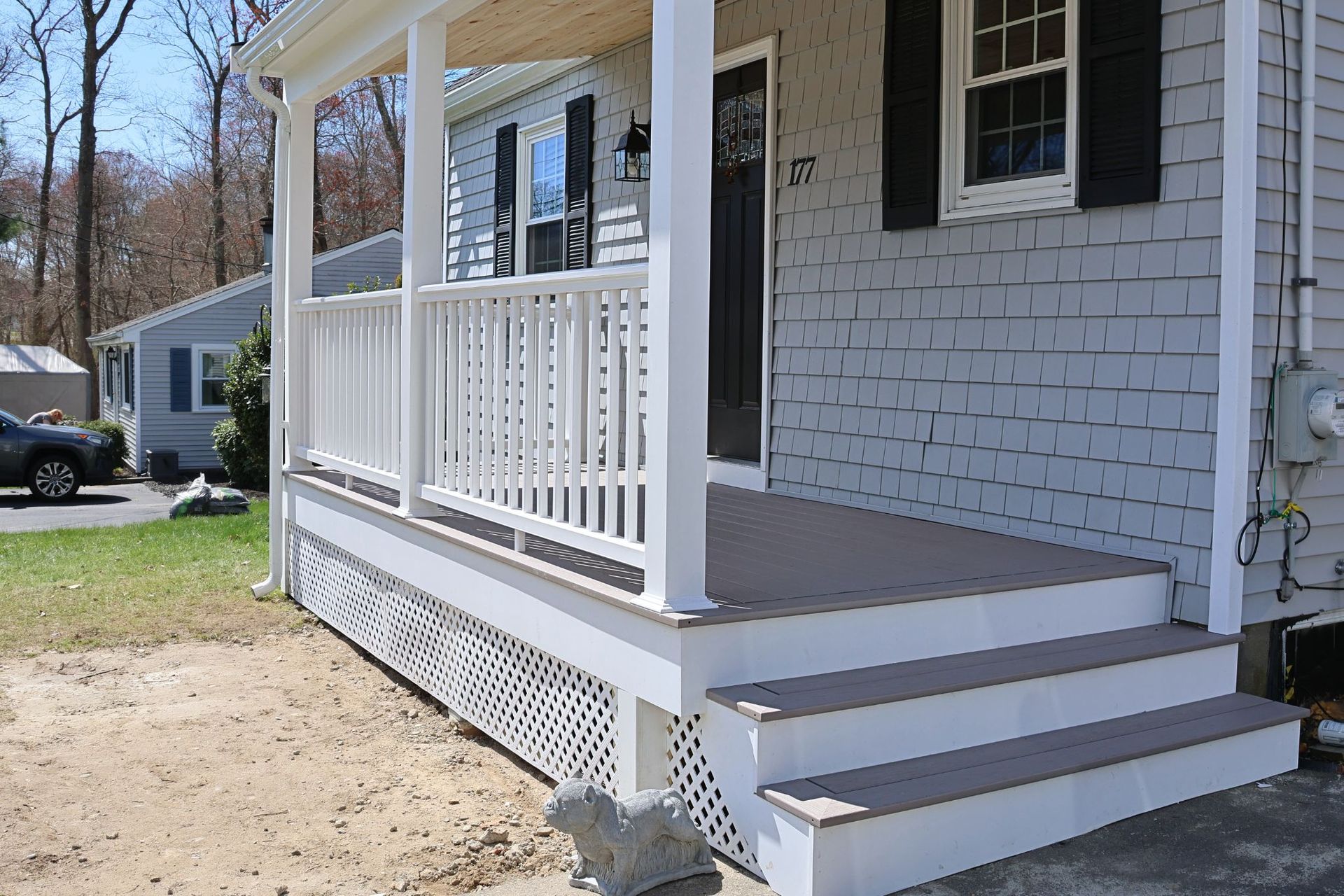 Front porch with white railing, gray steps, and a brick house exterior on a sunny day