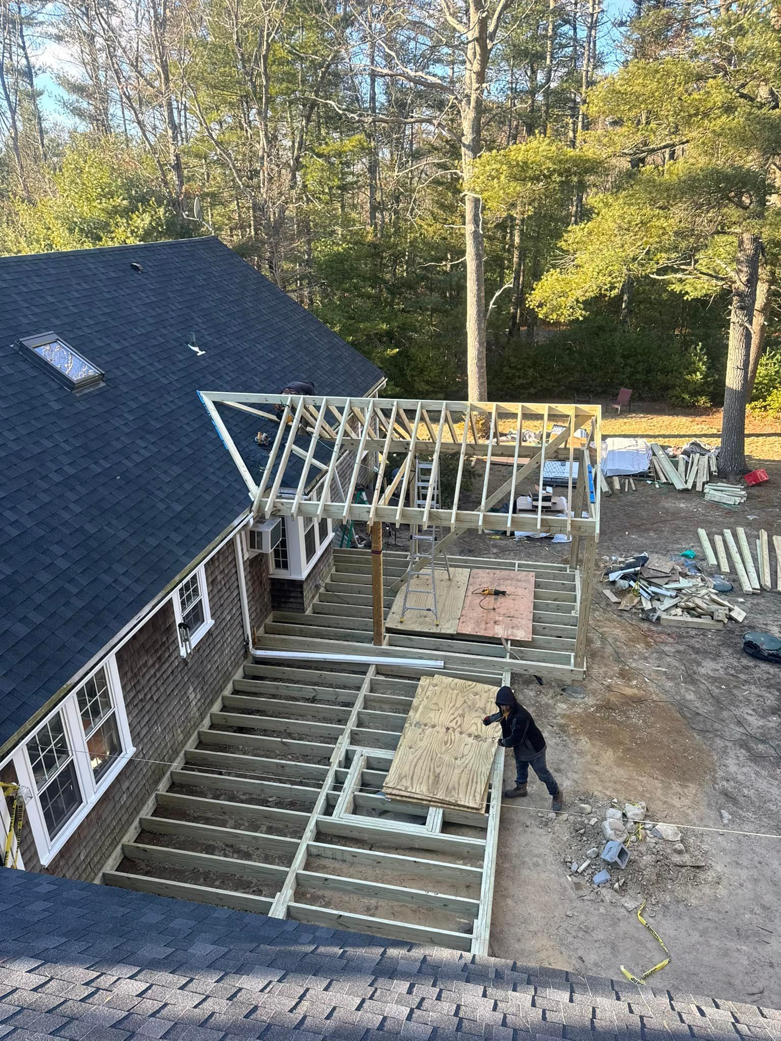 House under construction with roof framing and a worker beside a partially built deck