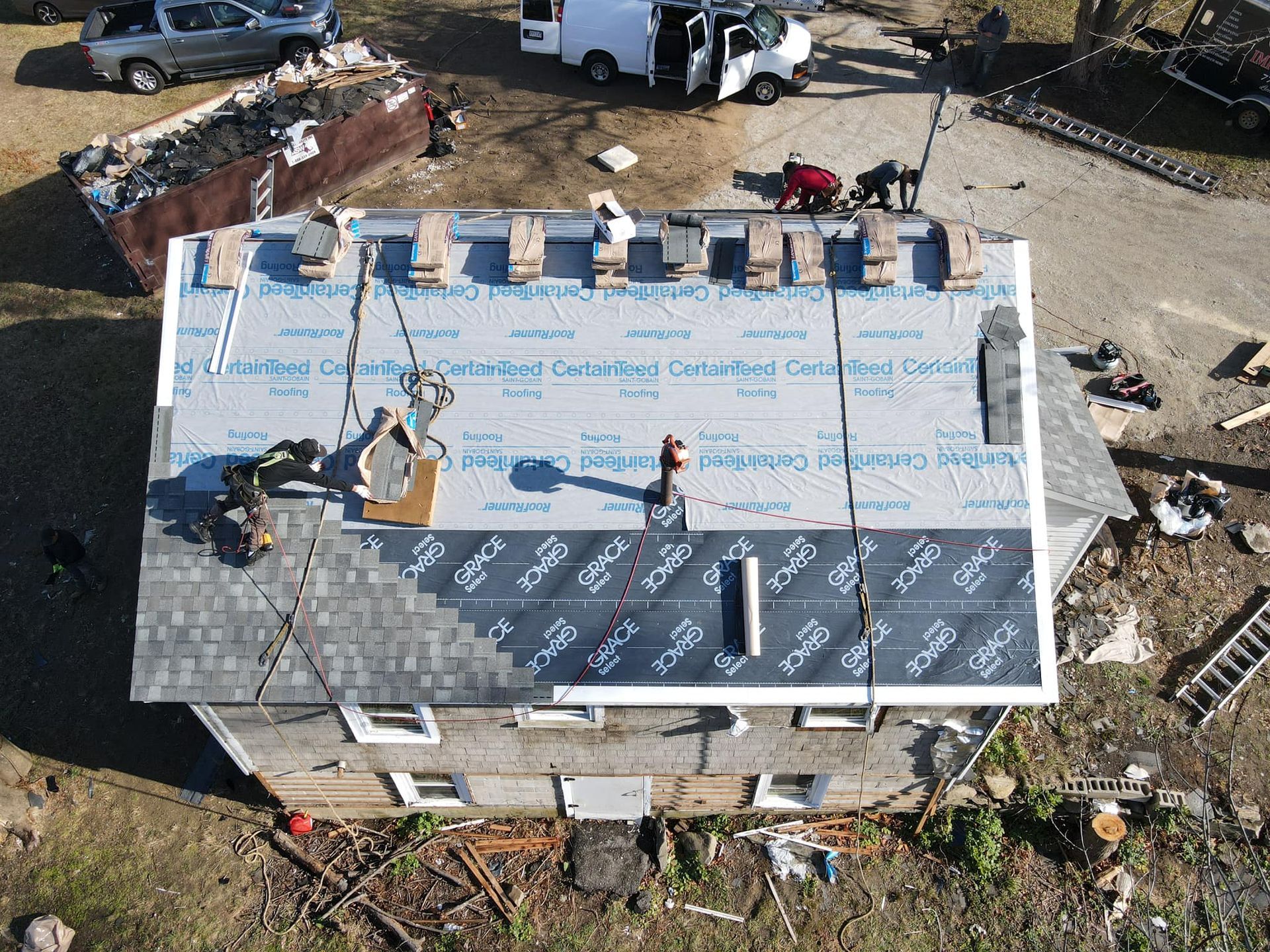 Aerial view of a house roof under construction with workers and materials on top.