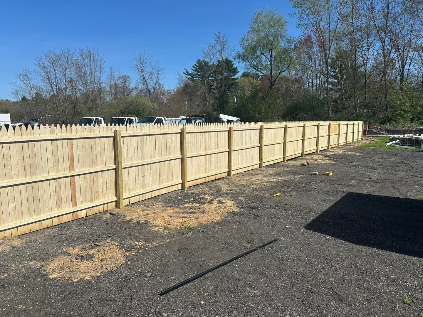 Wooden privacy fence along a gravel lot under a clear blue sky