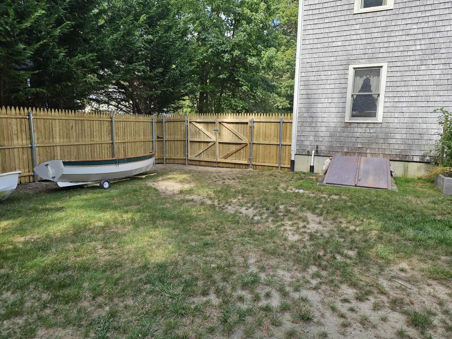 Backyard with wooden fence, grassy yard, small boat, and house siding with ramp.