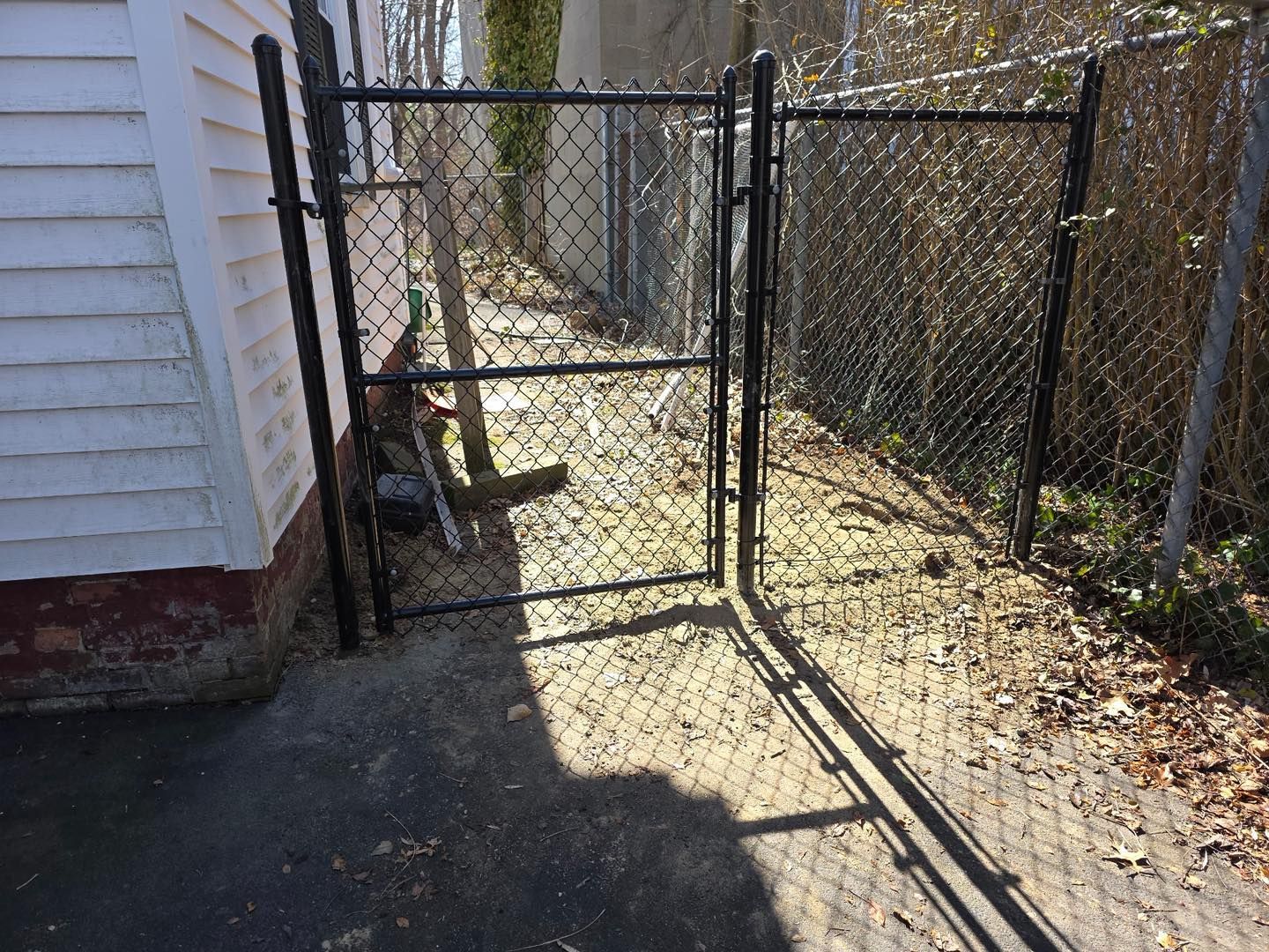 Open chain-link gate beside a white house, with a narrow concrete path and fence-lined yard.
