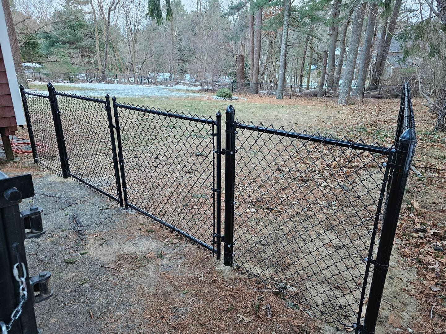 Black chain-link fence with a gate along a wooded yard in winter