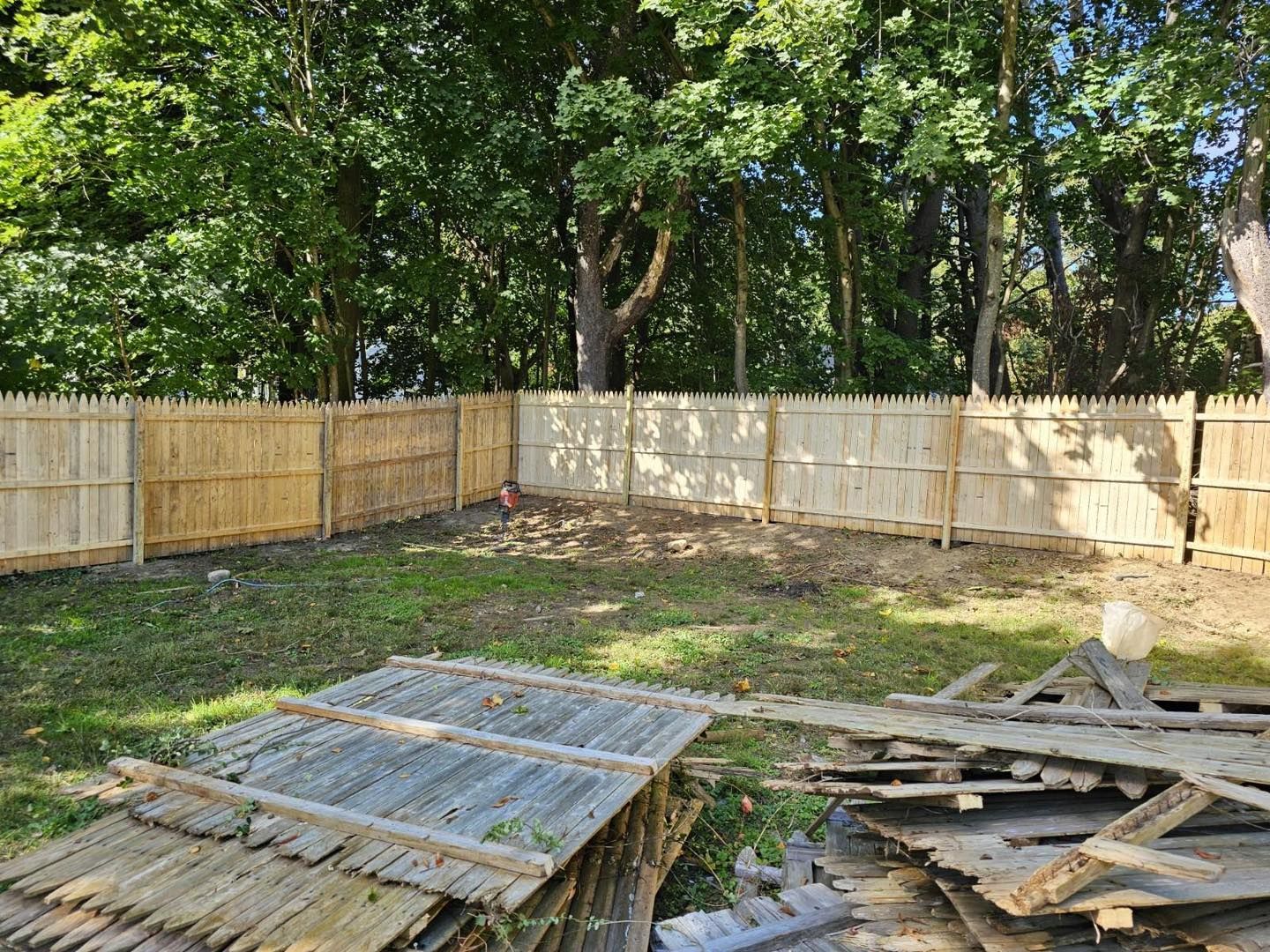 Backyard with a wooden fence, trees, and scattered construction debris on the ground.