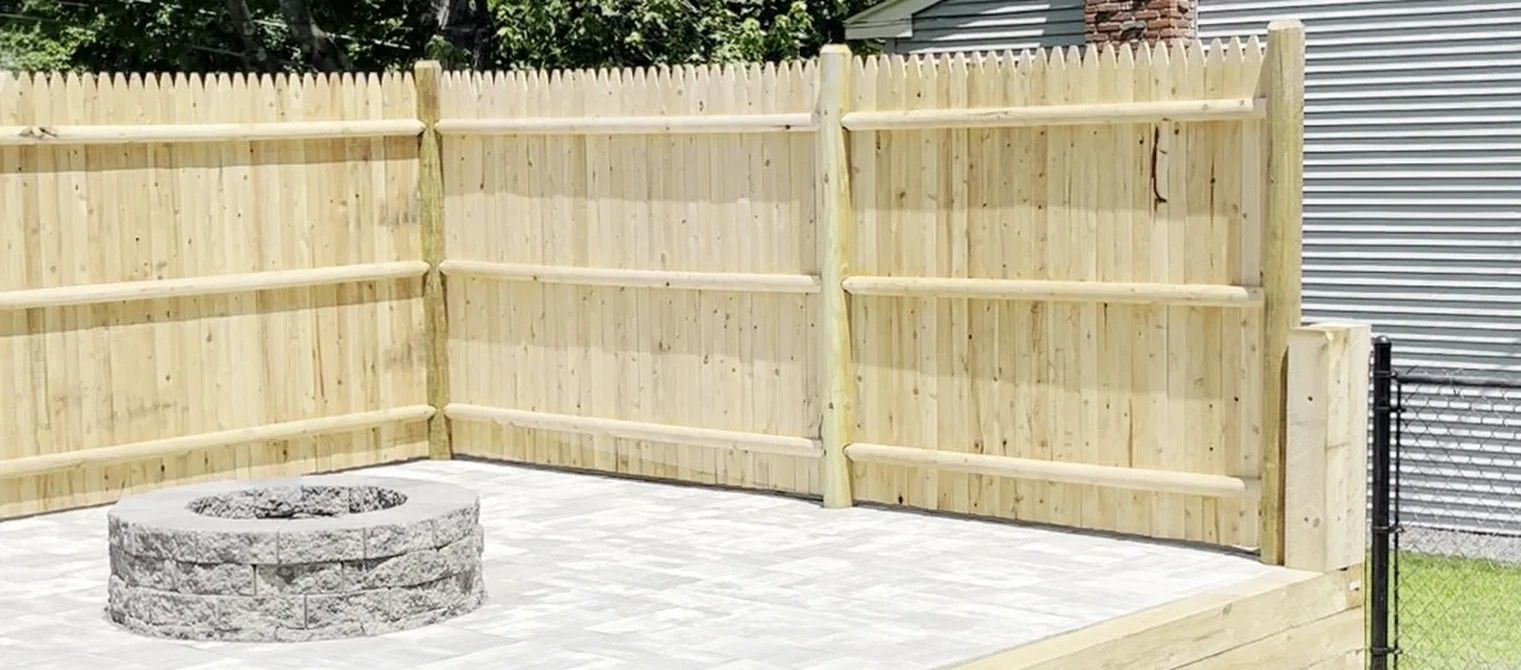 Backyard patio with a round stone fire pit and tall wooden privacy fence