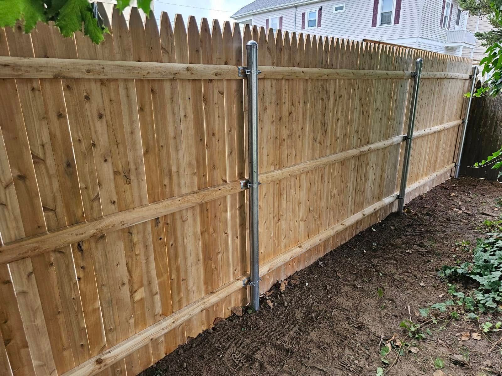 Wooden privacy fence with metal posts and dirt ground along a yard boundary