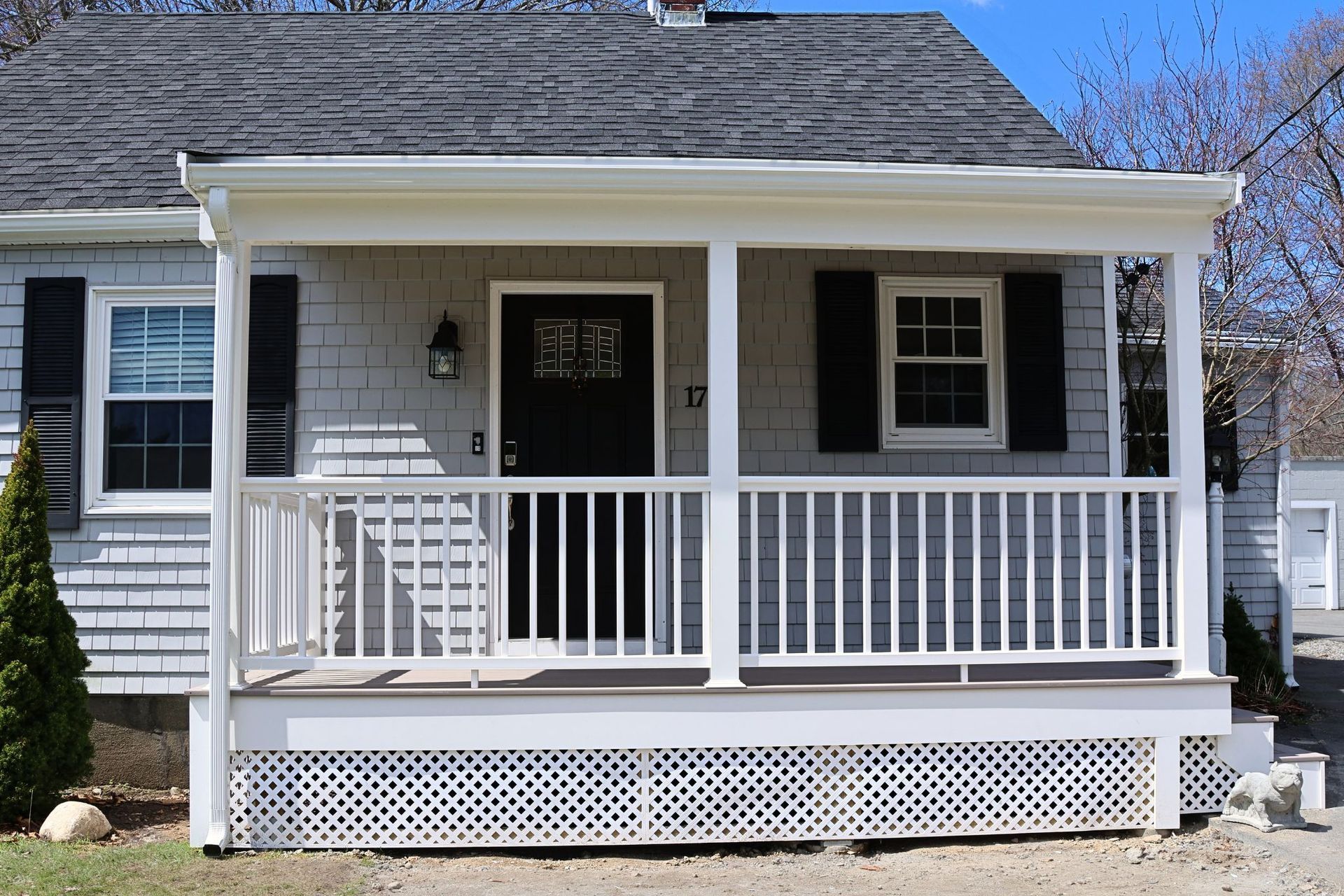 Small gray house with white porch railing and black shutters under a blue sky