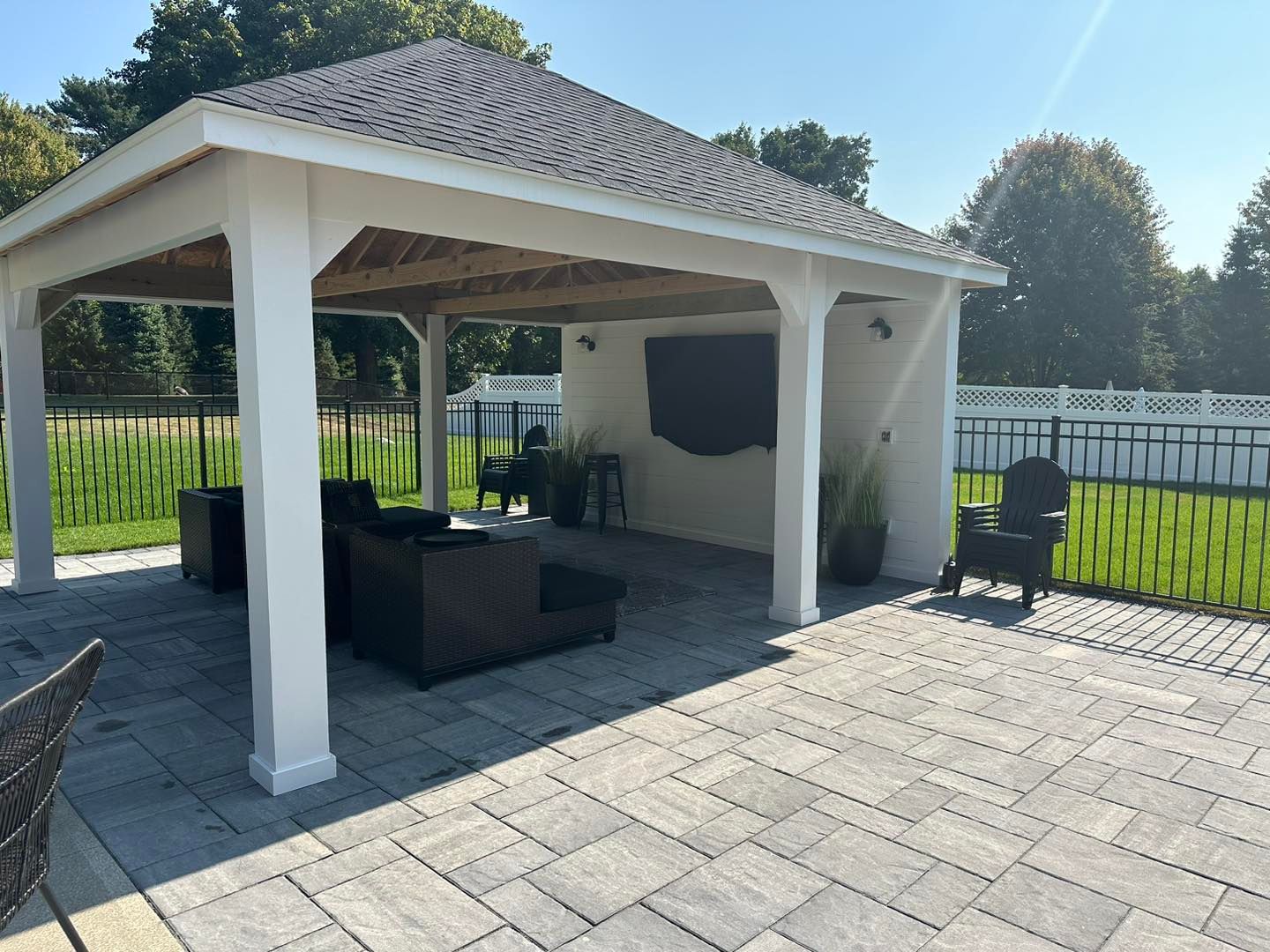 Covered patio gazebo with dark wicker seating on a paved backyard terrace