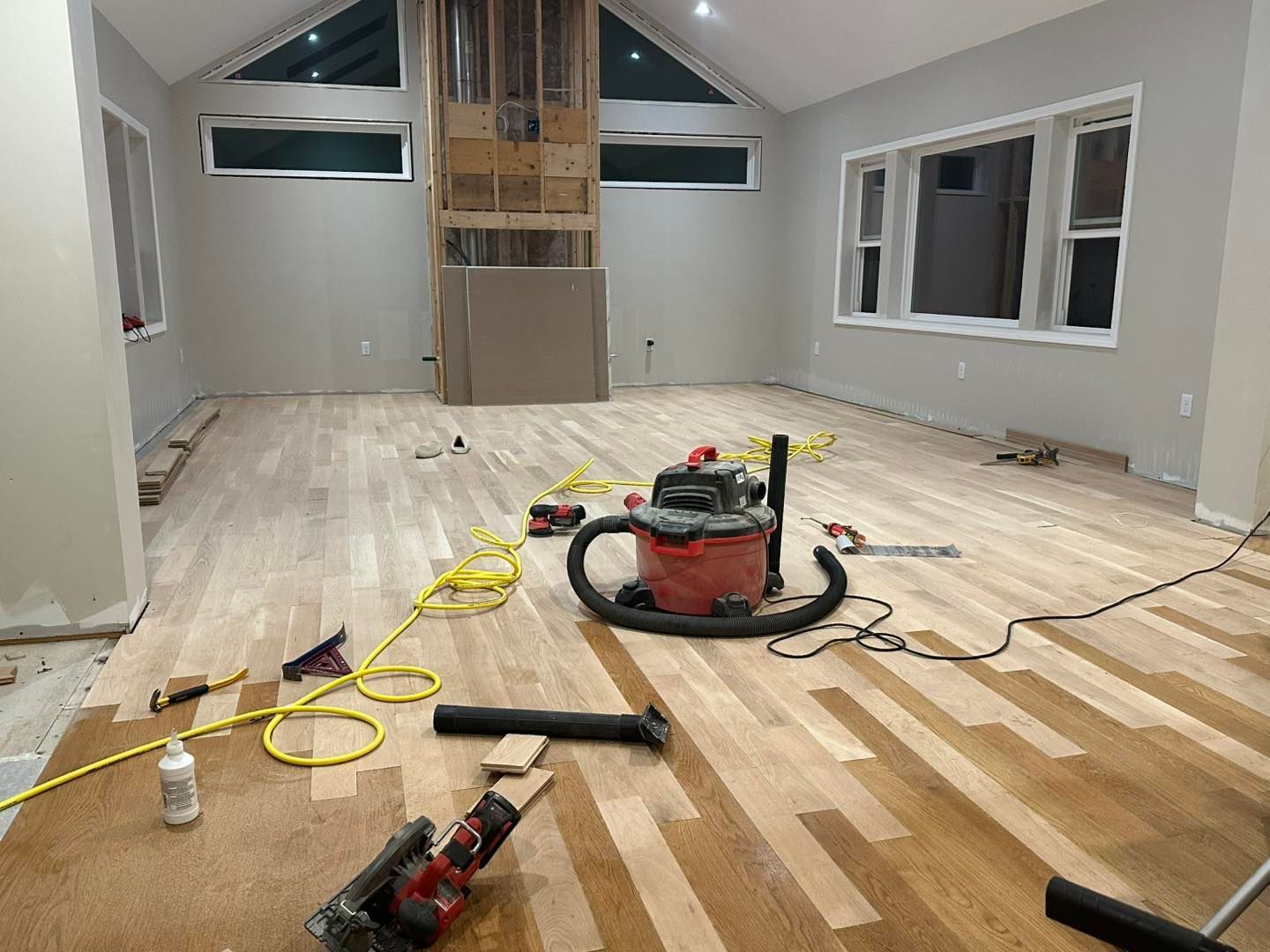 Dusty room under renovation with unfinished wood floor and a vacuum, tools, and cords scattered on the floor