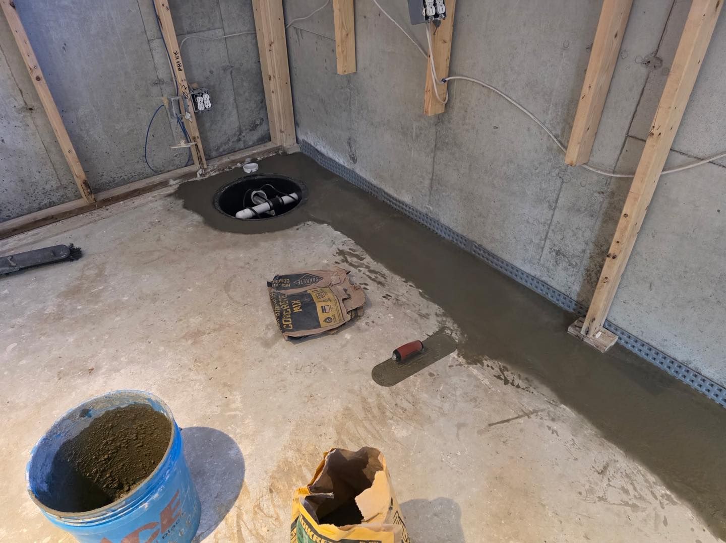 Concrete room under construction with a floor drain, bucket, tools, and unfinished walls