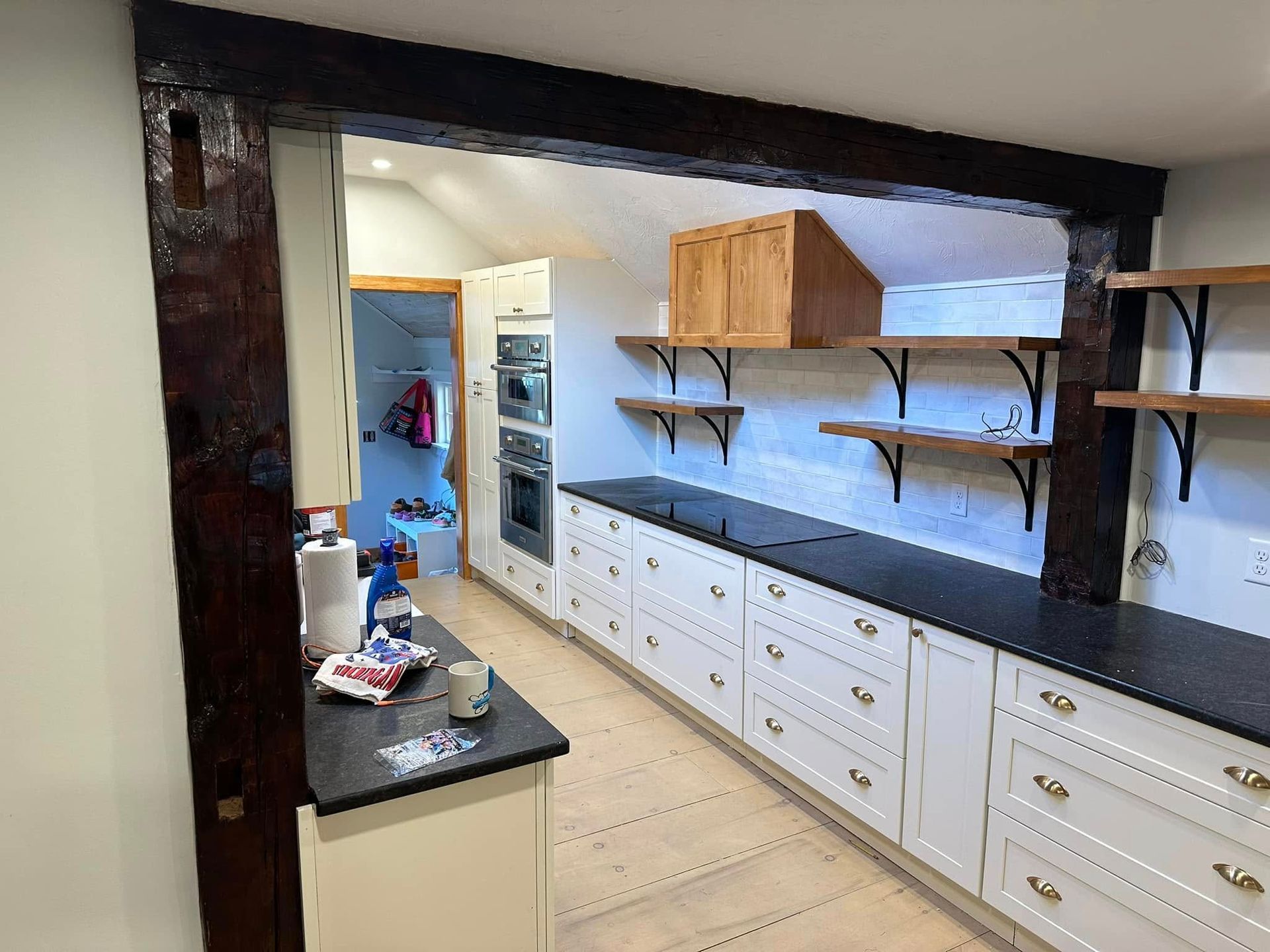 Long kitchen with white cabinets, black countertops, open shelves, and a doorway to another room.