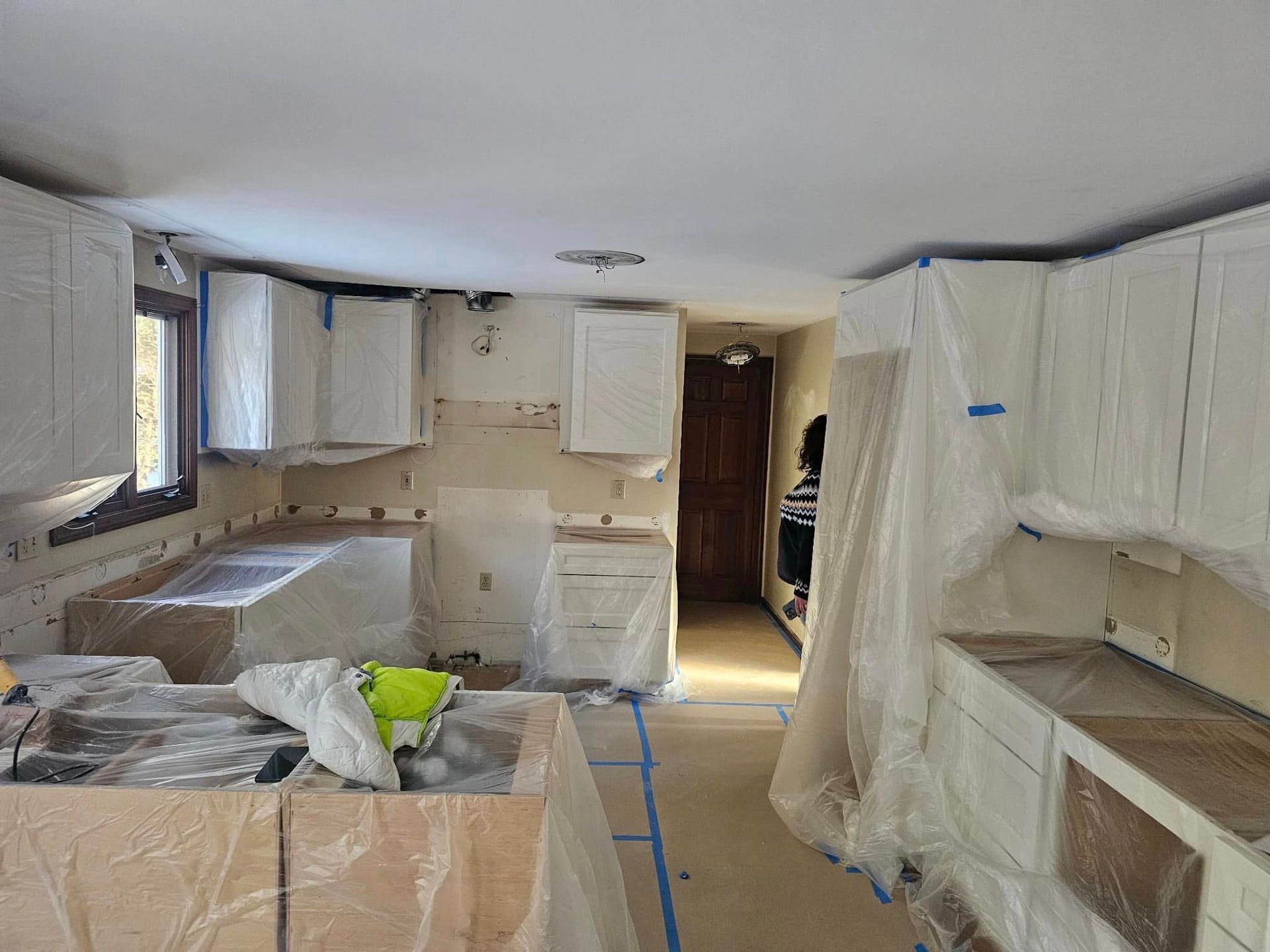 Kitchen under renovation, with cabinets covered in plastic and tools scattered around the room