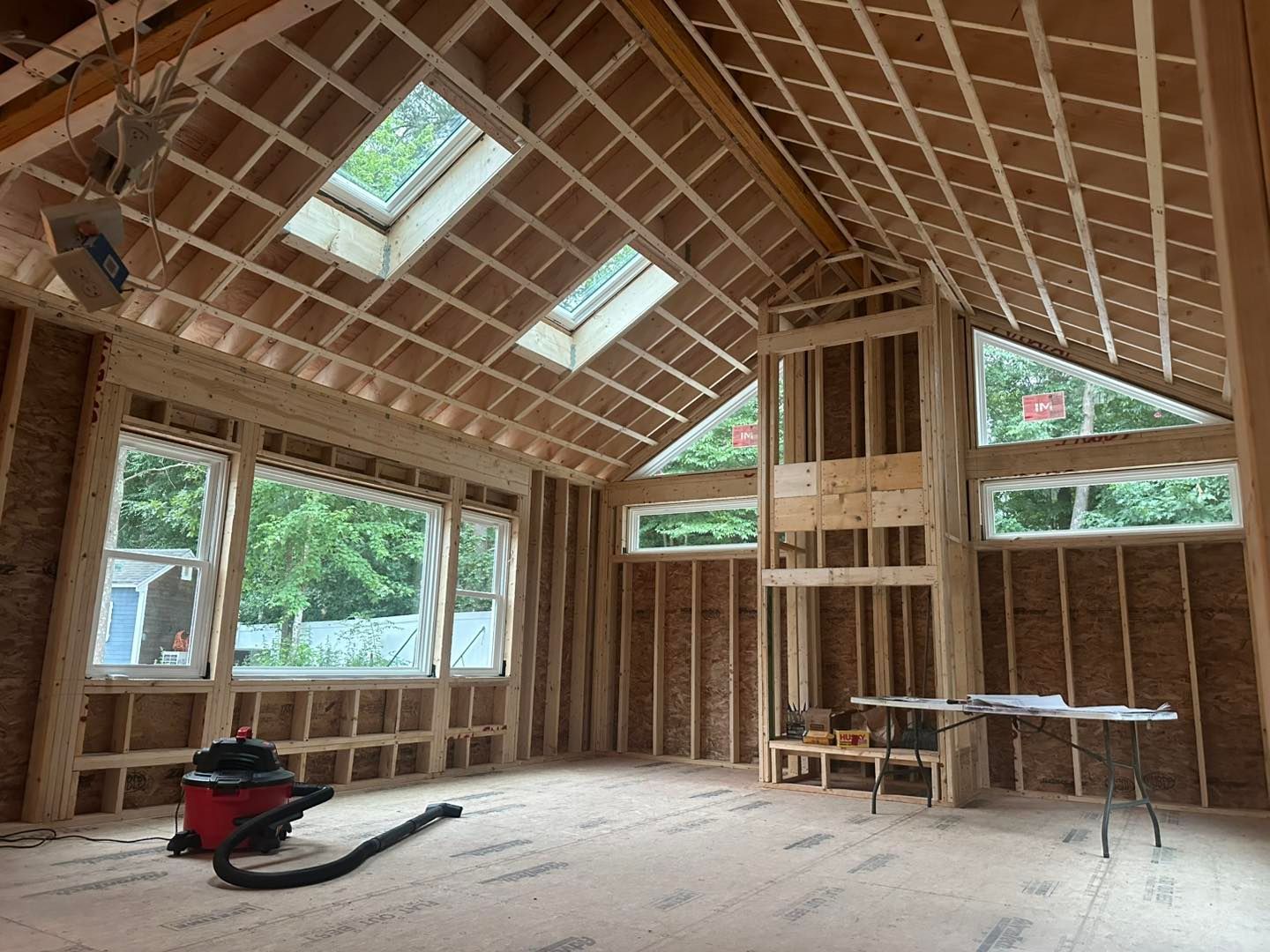 Unfinished wood-framed room with skylights, exposed rafters, and construction tools on the floor.