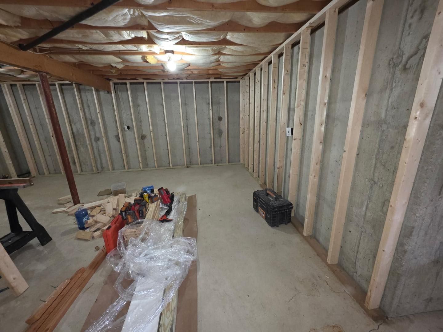 Basement under construction with exposed wall studs, insulation, and tools on the floor.