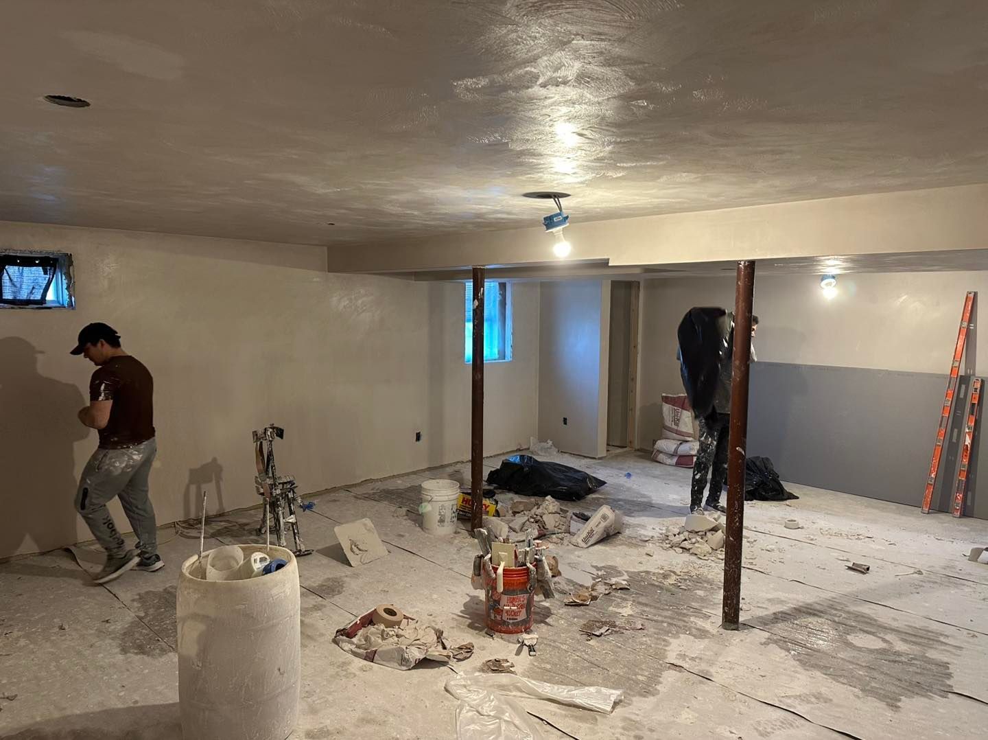 Construction worker in a room under renovation, with debris, tools, and unfinished walls.