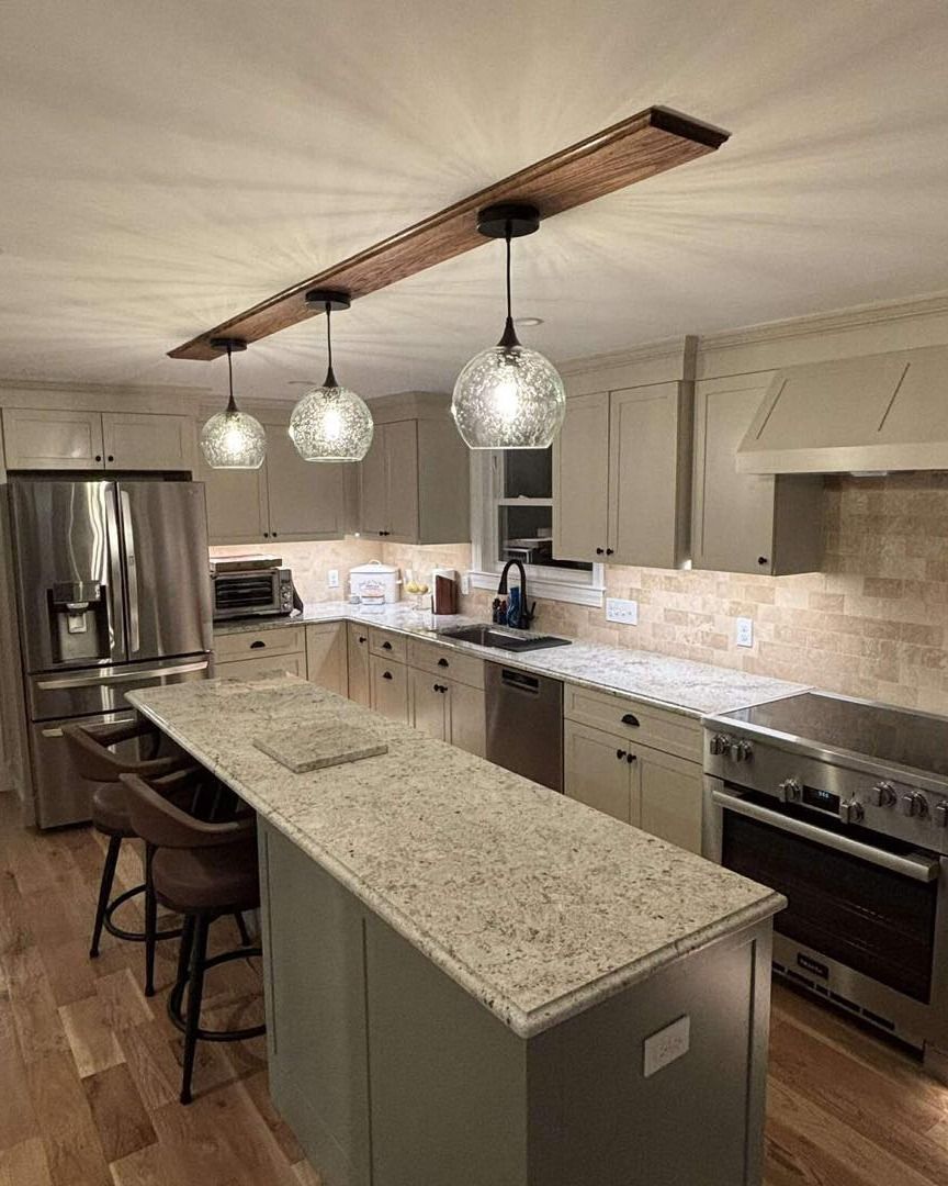Modern kitchen with granite island, pendant lights, stainless appliances, and wood flooring.