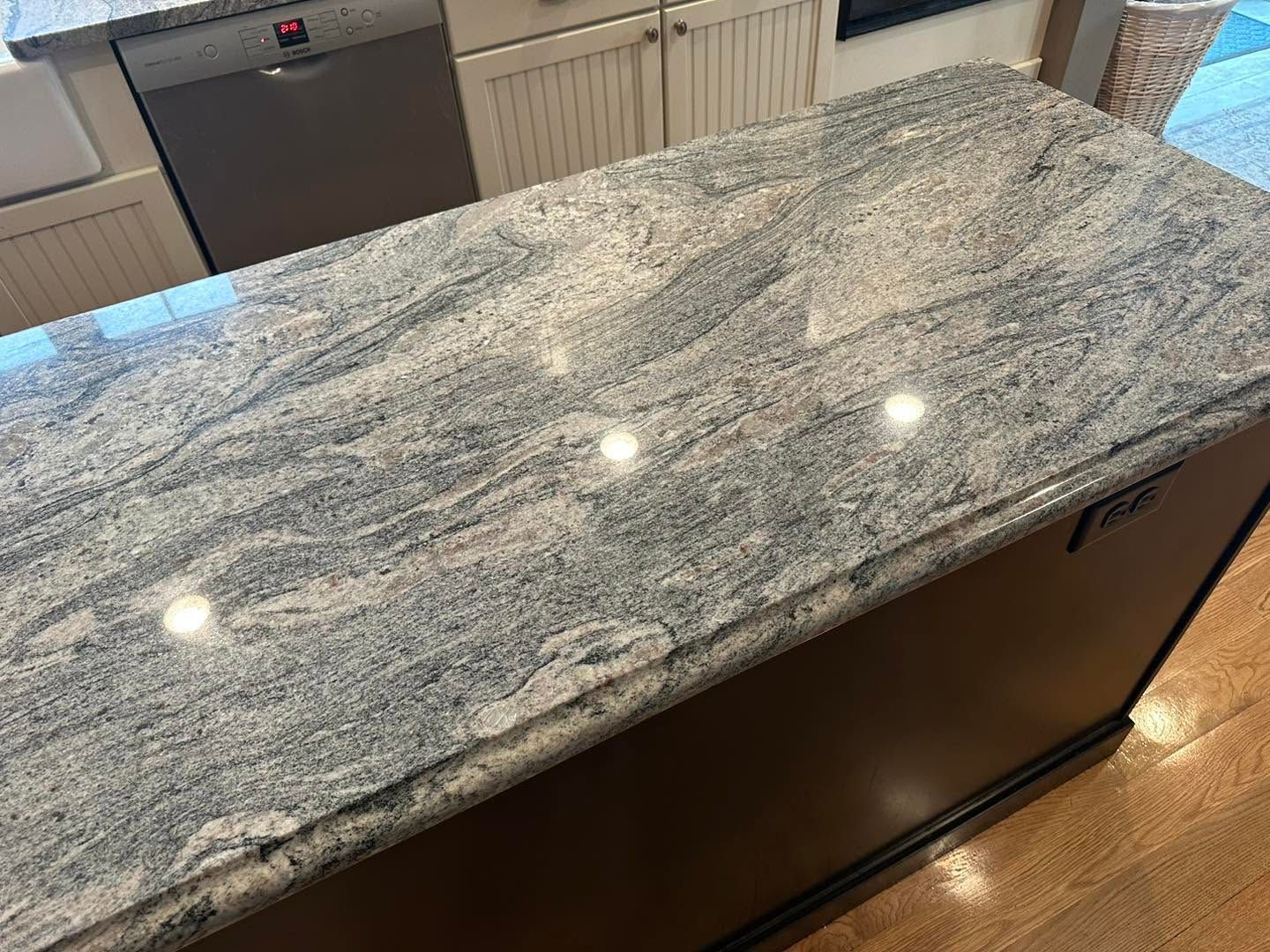 Granite kitchen island countertop with light gray and black veining under recessed lights