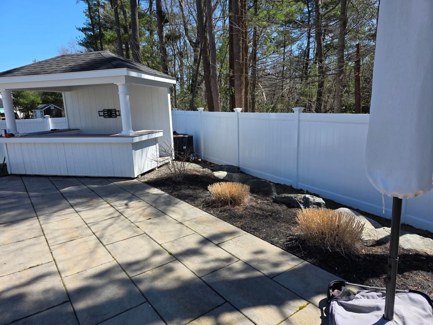 Backyard patio with white gazebo, fence, trees, and potted plants in bright sunlight