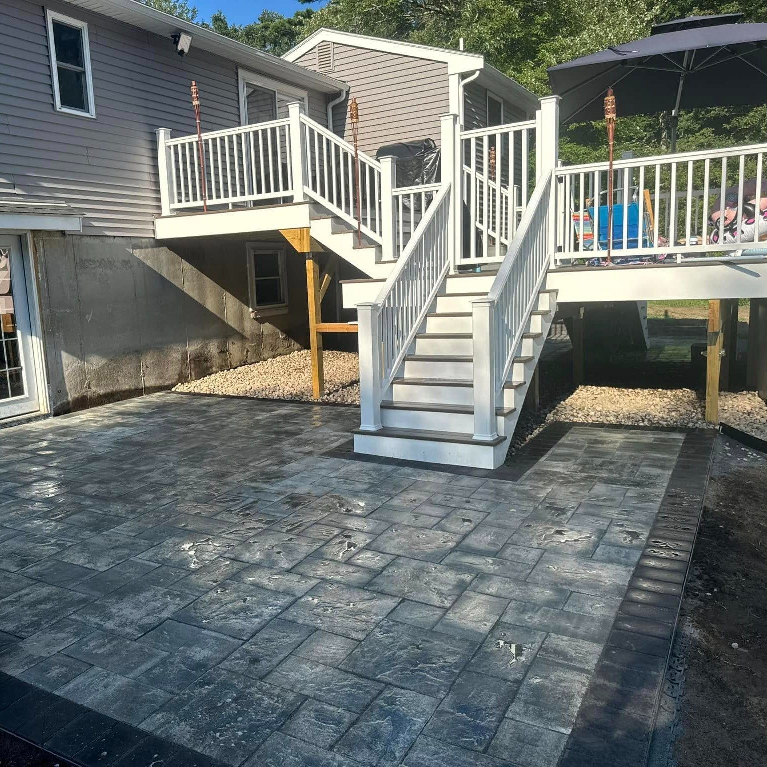 Backyard deck with white stairs descending to a stone patio beside a gray house