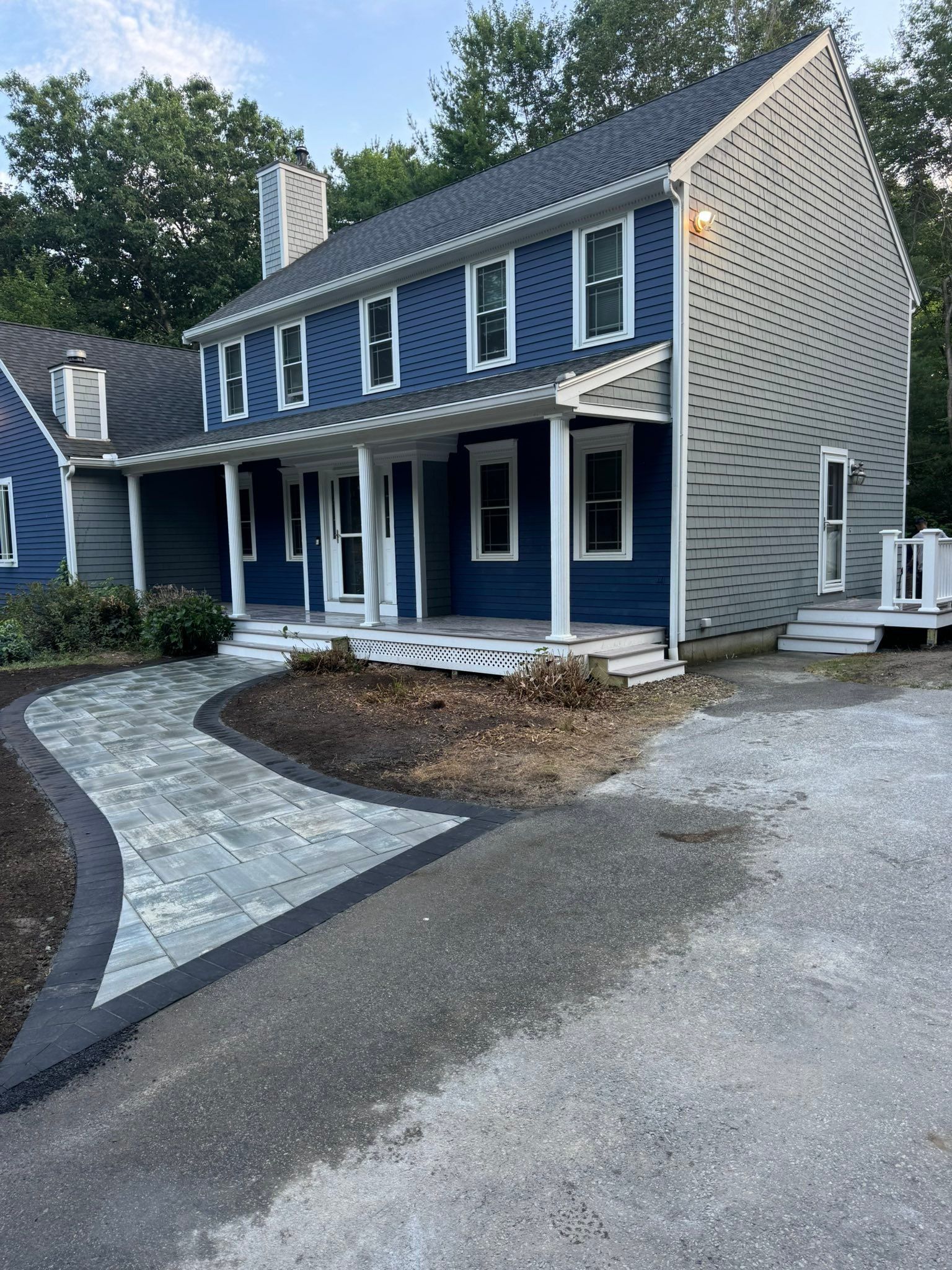 Blue two-story house with white trim, front porch, curved walkway, and gravel driveway at dusk