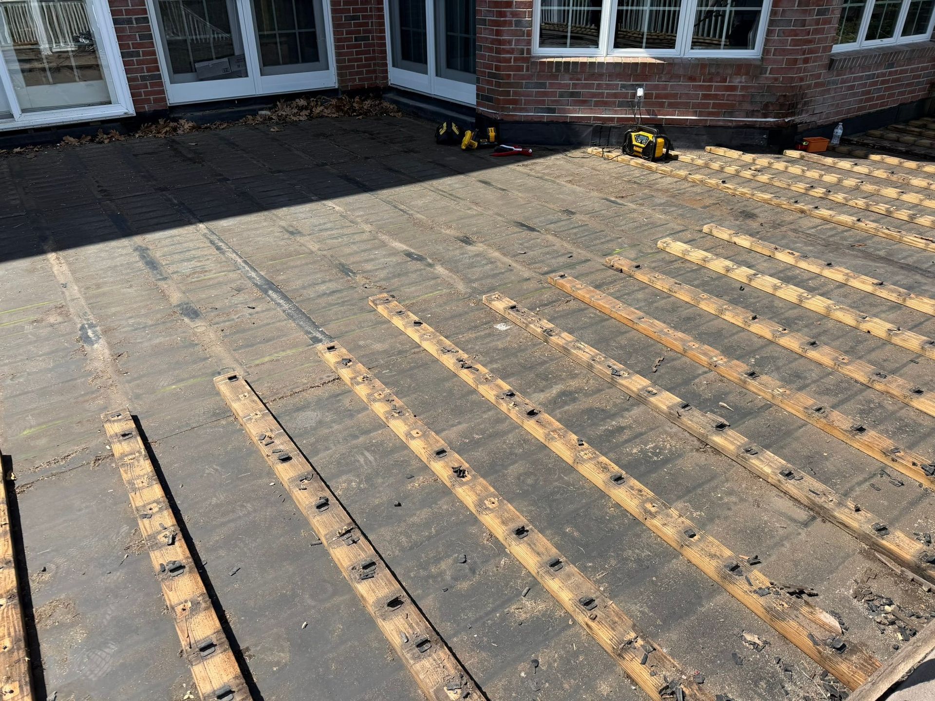 Partially built wooden deck framing beside a brick house, with tools near the back wall.
