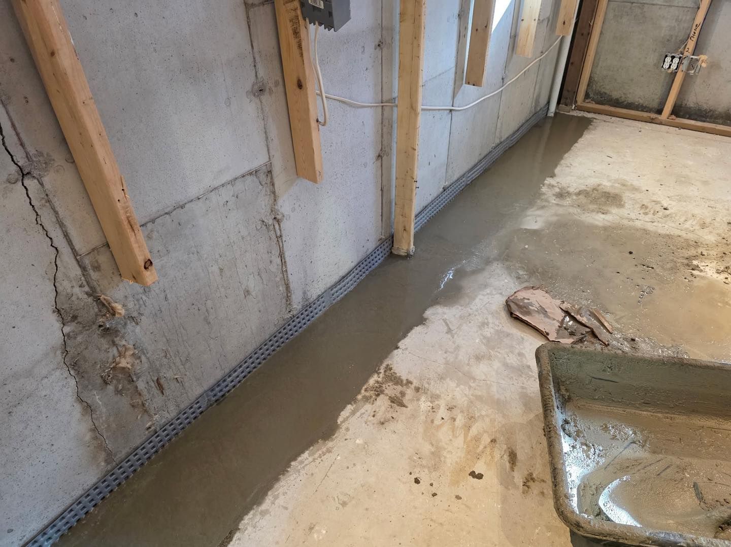 Wet basement floor with standing water along unfinished concrete walls and wood framing