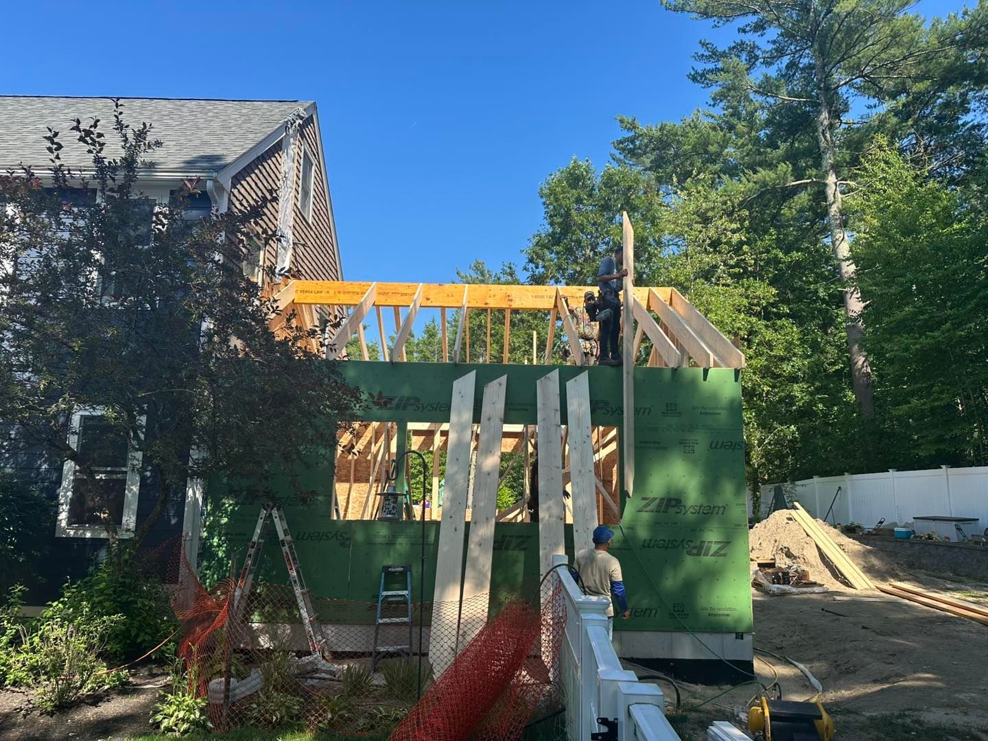 Green house under construction with exposed framing and workers on a sunny day