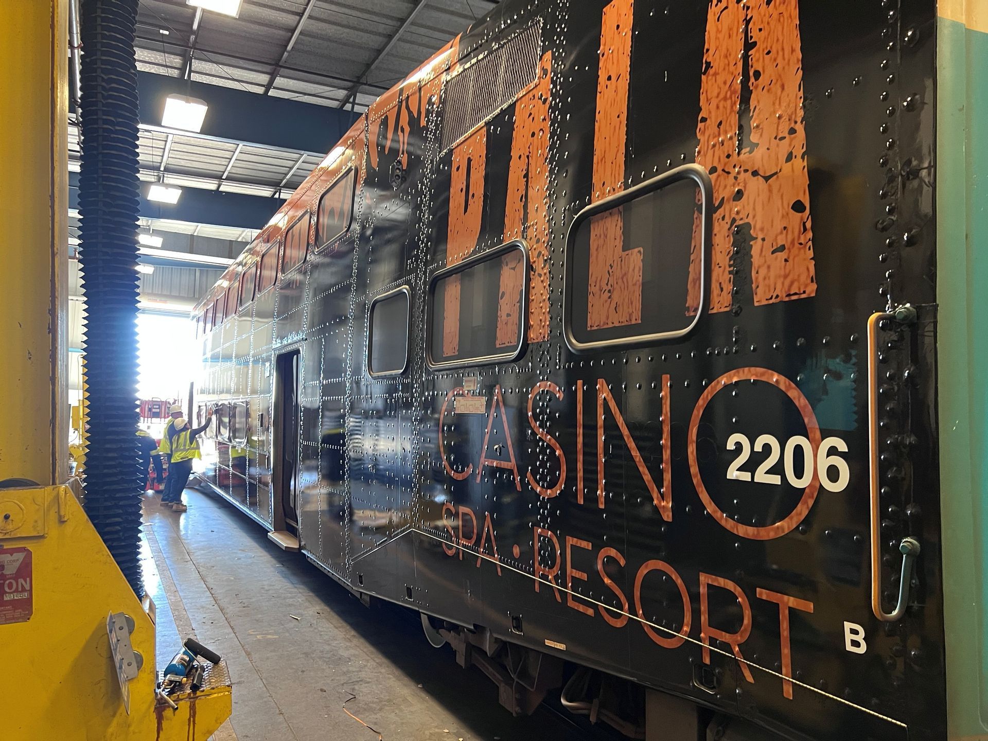 Side view of a double-decker train car in a garage, black with orange text: 