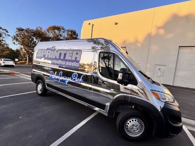 Shiny silver Sprinter van parked in lot with logo 