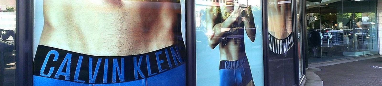 A storefront featuring Calvin Klein underwear ad. A person's stomach with a Calvin Klein waistband.